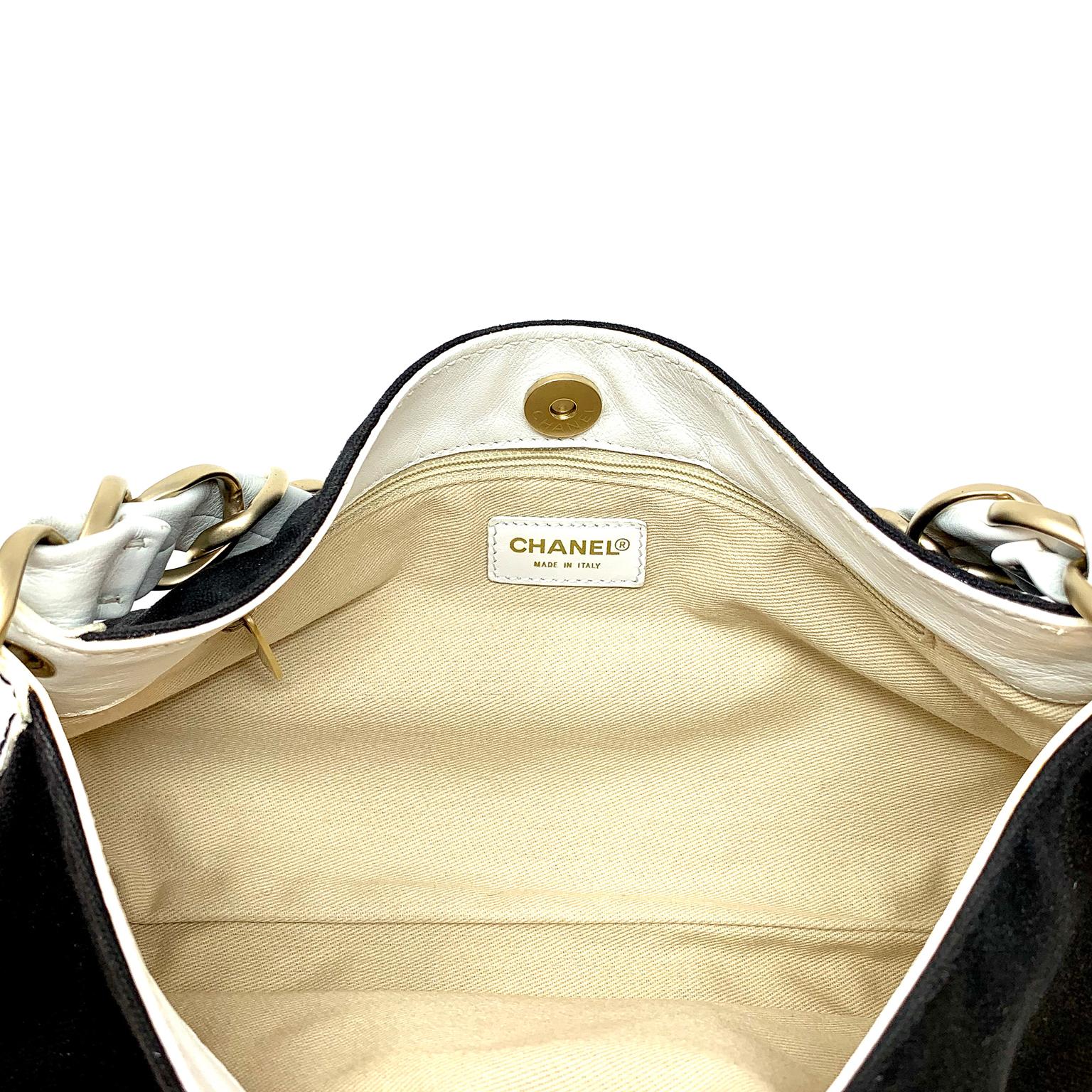 Cet authentique sac à bandoulière Chanel en toile noire est en excellent état.  Toile noire avec surpiqûres ton sur ton et coins renforcés en cuir blanc.  Le bracelet simple en cuir blanc est entrelacé avec une chaîne en or mat.  La fermeture