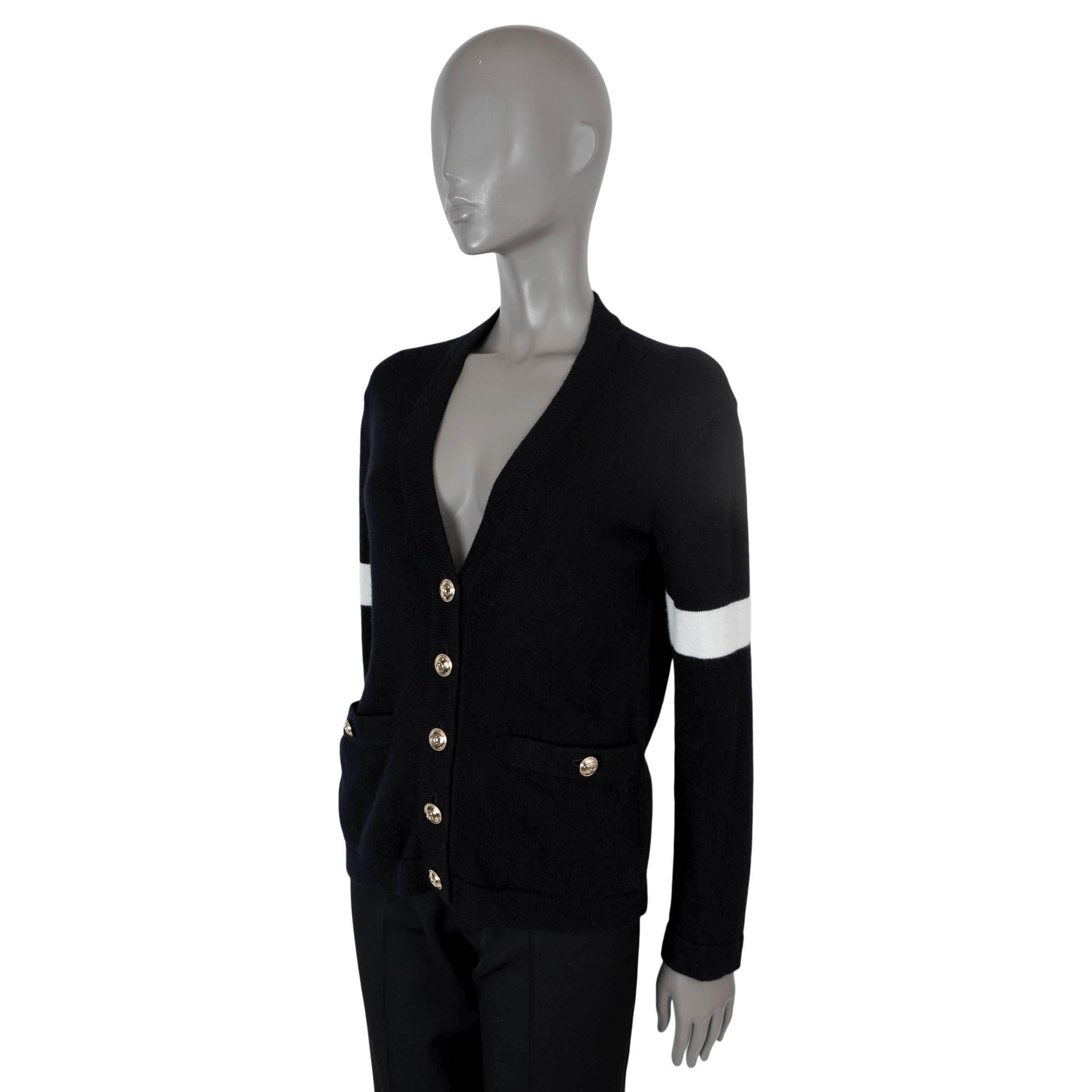 Cárdigan de cuello de pico 100% auténtico Chanel de cachemira negra (100%). Presenta rayas marfil en las mangas, ribetes de punto elástico y bolsillos abotonados en la cintura. Se cierra con botones CC dorados y no lleva forro. Se ha usado y está en