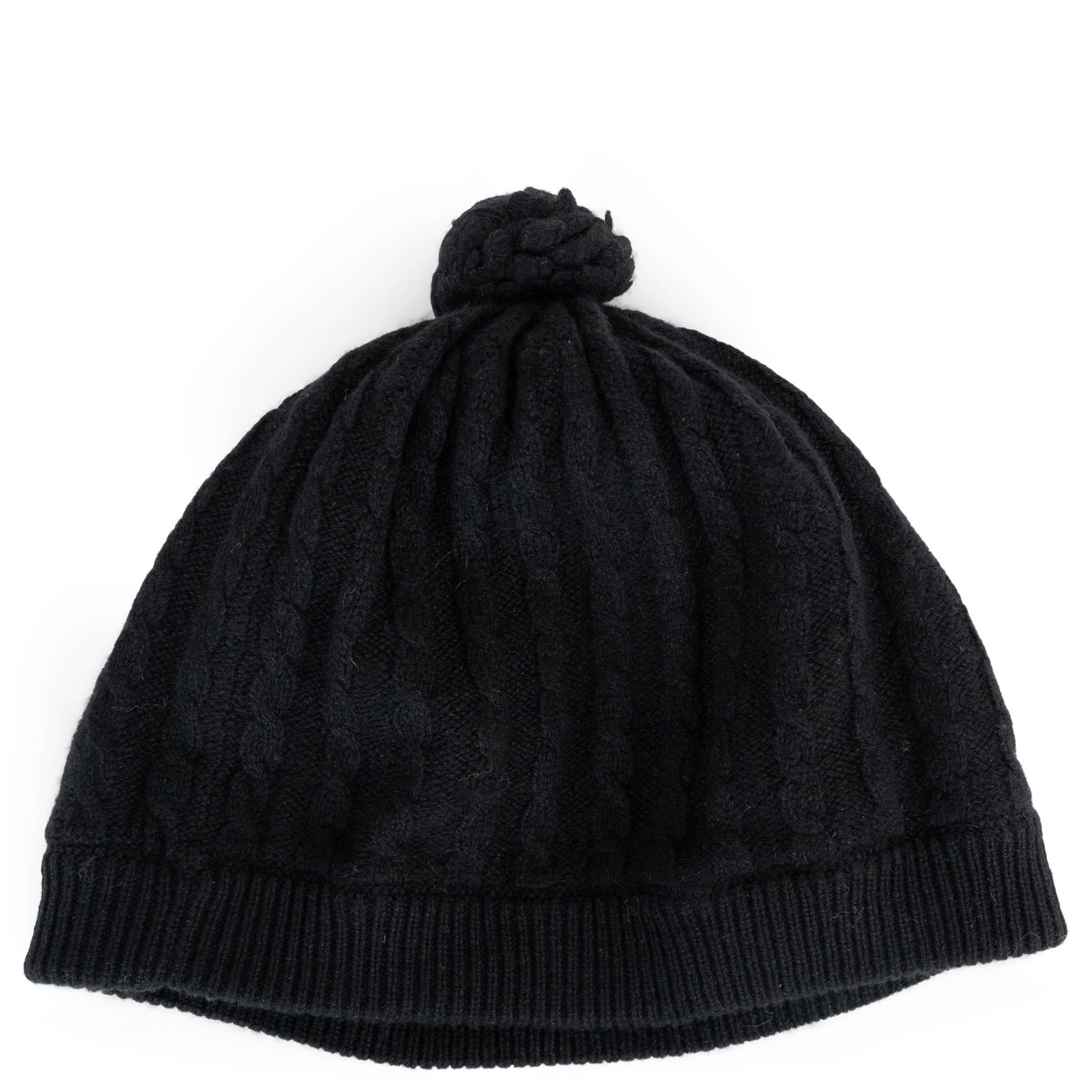 Ce bonnet Chanel 100 % authentique est confectionné en cachemire noir tricoté par câble pour une sensation de peluche et de confort. Il arbore un logo CC embelli par des chaînes et des perles, un pompon ludique sur le dessus et des bordures en