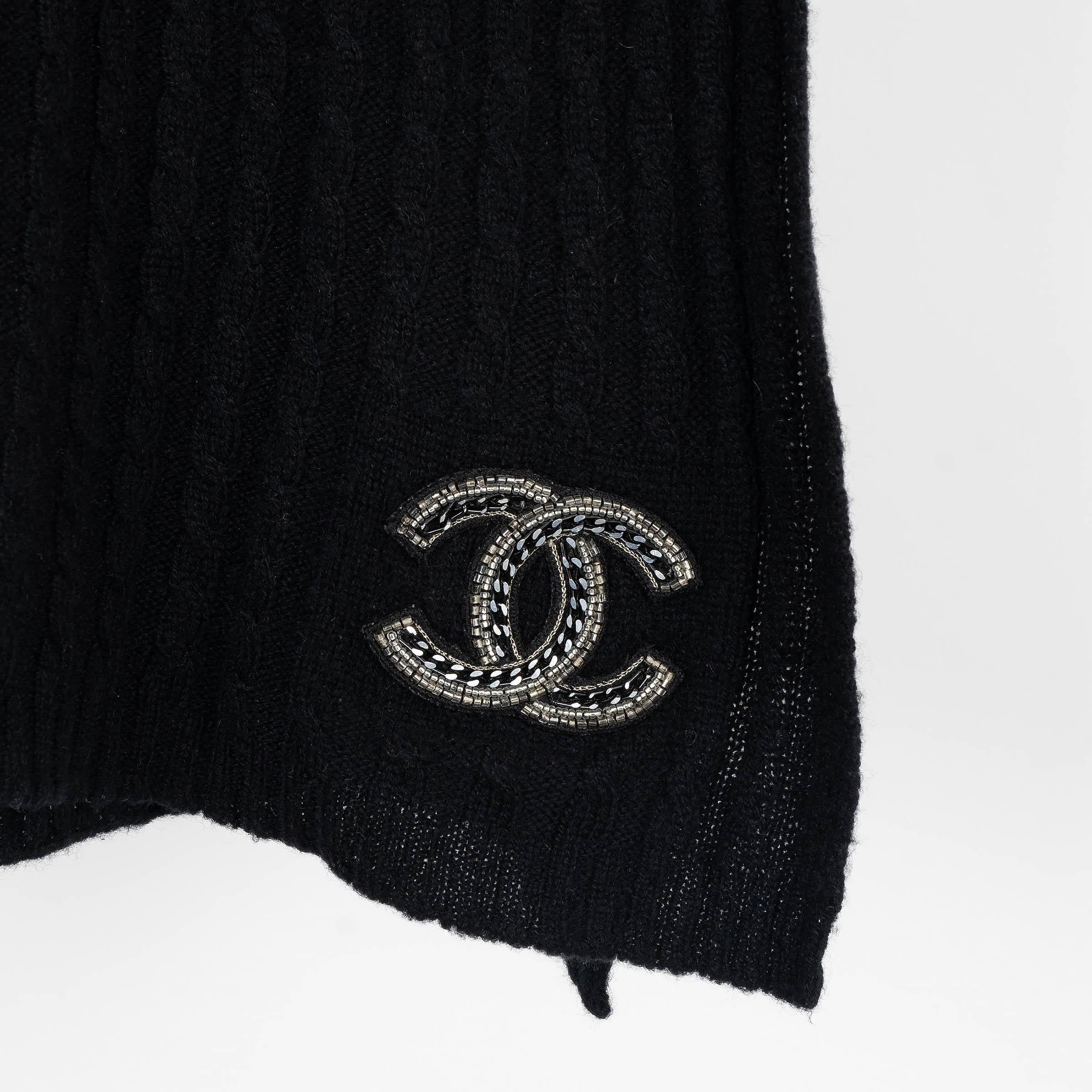 Questa muffola Chanel, autentica al 100%, è realizzata in cashmere nero lavorato a maglia a cavo per una morbidezza e un calore eccezionali. Presenta l'iconico logo CC impreziosito da catene e perline che aggiungono un tocco di eleganza. Rifinito