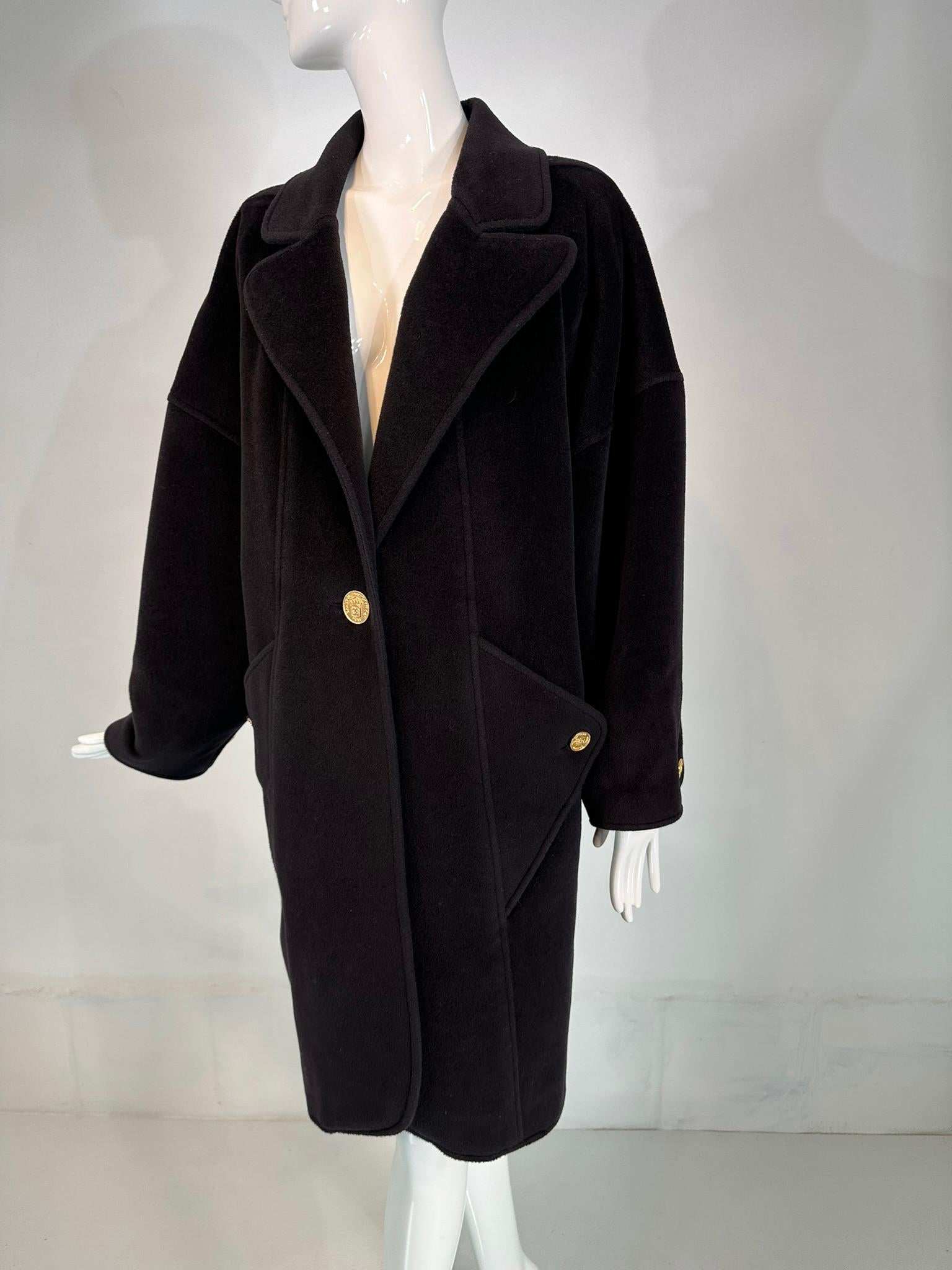 Cappotto Chanel 1988 in cachemire nero con tasche anteriori con bottoni a triangolo. Il cappotto a forma di cocomero ha lunghi revers dentellati e si chiude sul davanti con un unico bottone con logo. Le maniche lunghe hanno i polsini curvi e i