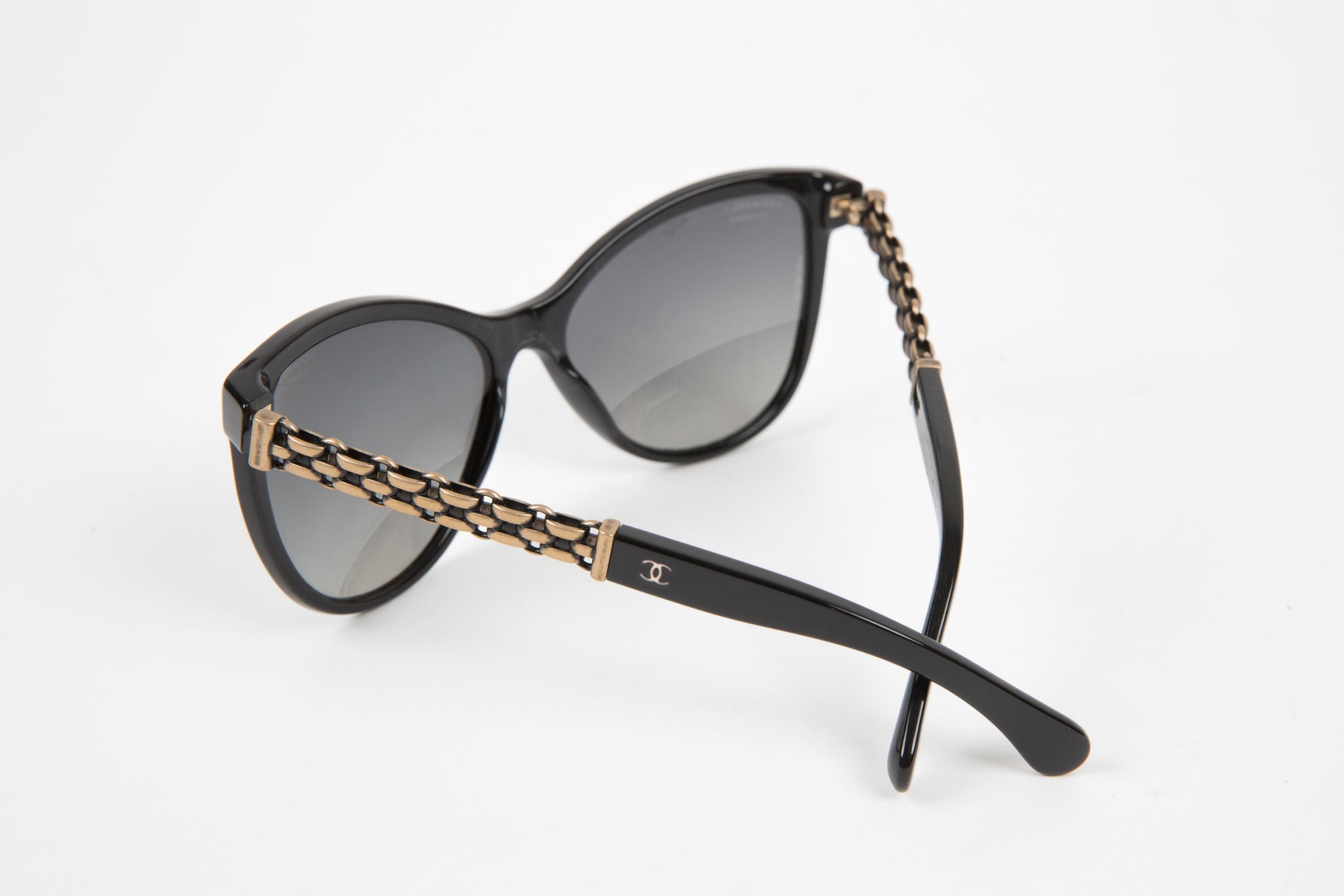 Schwarze Cat-Eye-Sonnenbrille aus Acetat von Chanel mit folgenden Eigenschaften: mattgoldene Kette und Chanel-Signatur am Bügel, Cat-Eye-Rahmen, gerade Bügel mit gebogenen Spitzen.
100% Acetat. Um die 2000er Jahre.   
Armlänge 14 cm