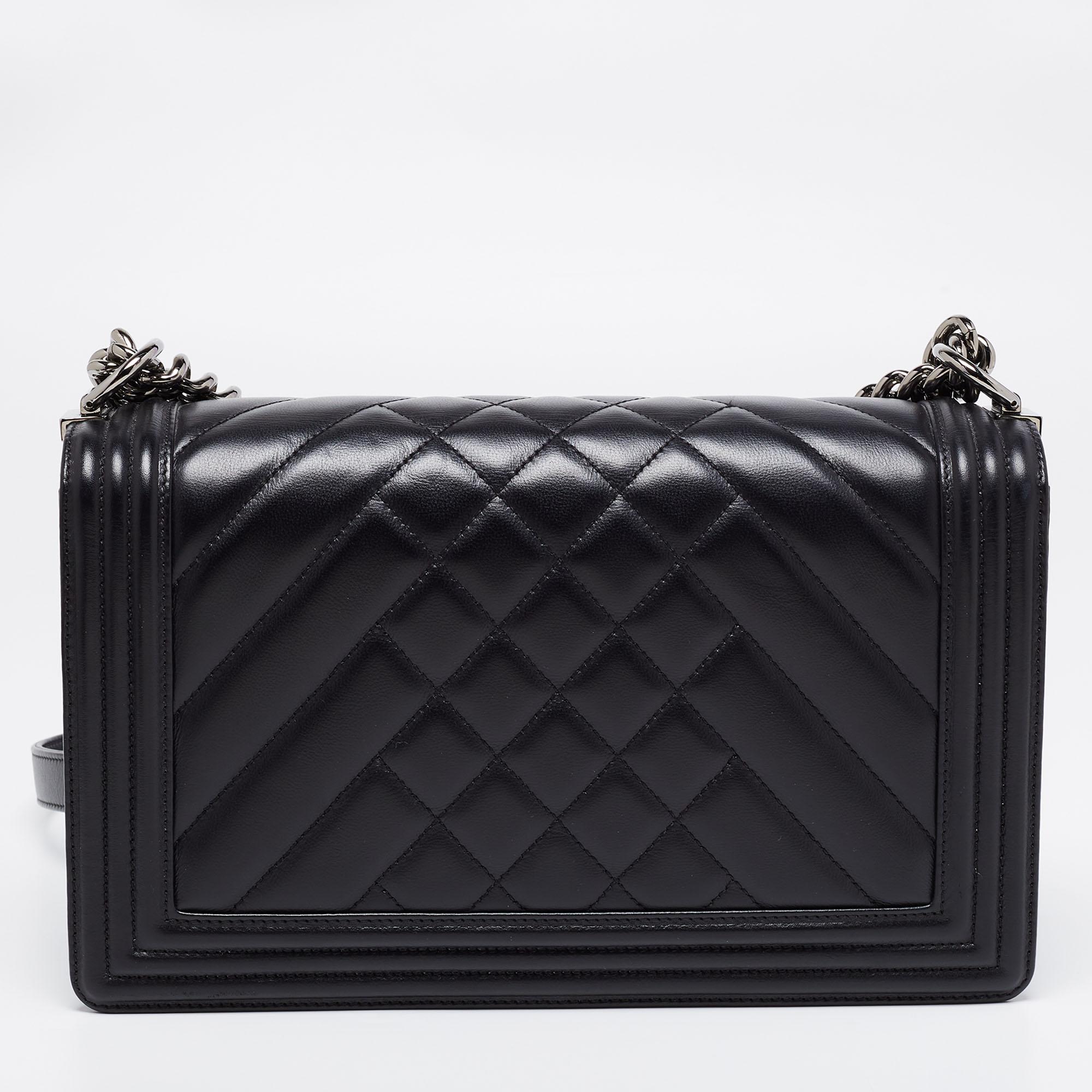 The New Medium Boy Flap Bag is another prized handbag by Chanel. Here is a version in black leather with the iconic CC push lock on the flap and a mix of chevron & diamond quilt on the exterior. The piece has gunmetal-tone hardware, and a chain-link