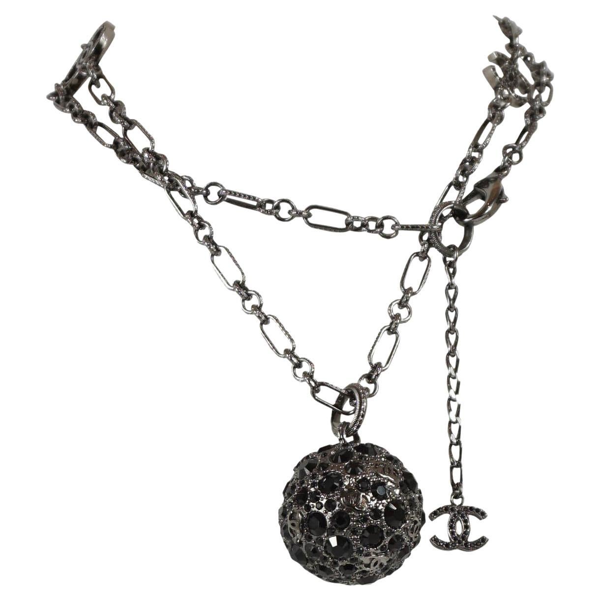 Chanel necklace, from their 2007 Autumn Collection, features a black strass chain with a blackened silver ball pendant encrusted with black crystals and an interlocking CC logo. Chain has gunmetal hardware, interlocking CC logos and black strass