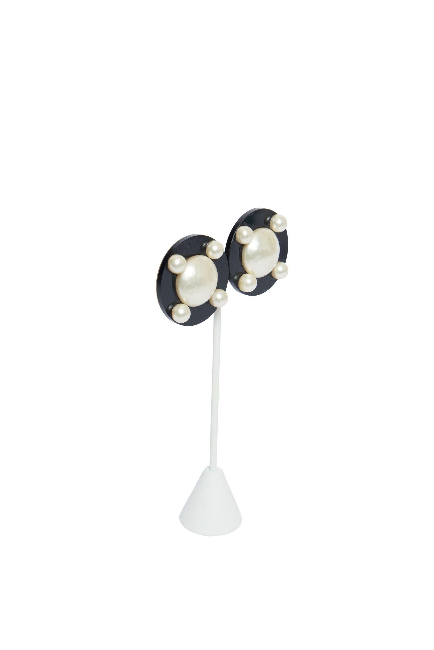 Schwarze Chanel Clip-Ohrringe aus Lucite mit einer großen Perle in der Mitte. Auf der Blende sind vier Perlen zu sehen und der Durchmesser beträgt 1,6'. Auf der Rückseite der Ohrringe befindet sich ein Goldplättchen, das die Echtheit bestätigt.