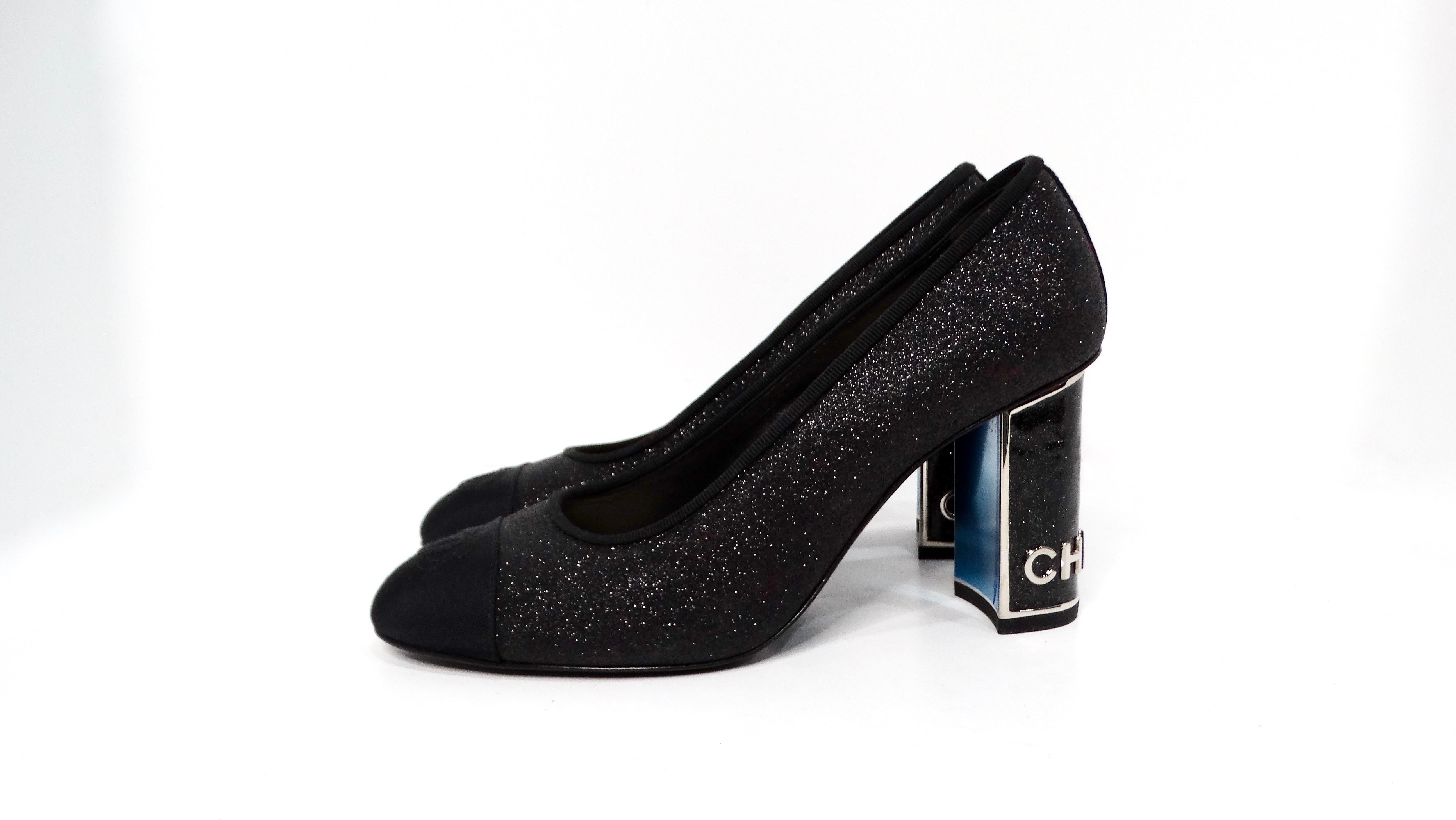 Step into elegance with the Chanel Black Glitter Grosgrain Cap Toe Logo Pumps, a stunning addition to any fashionista's wardrobe. These chic pumps showcase a dazzling black glitter exterior that shimmers with every step you take. The sophisticated