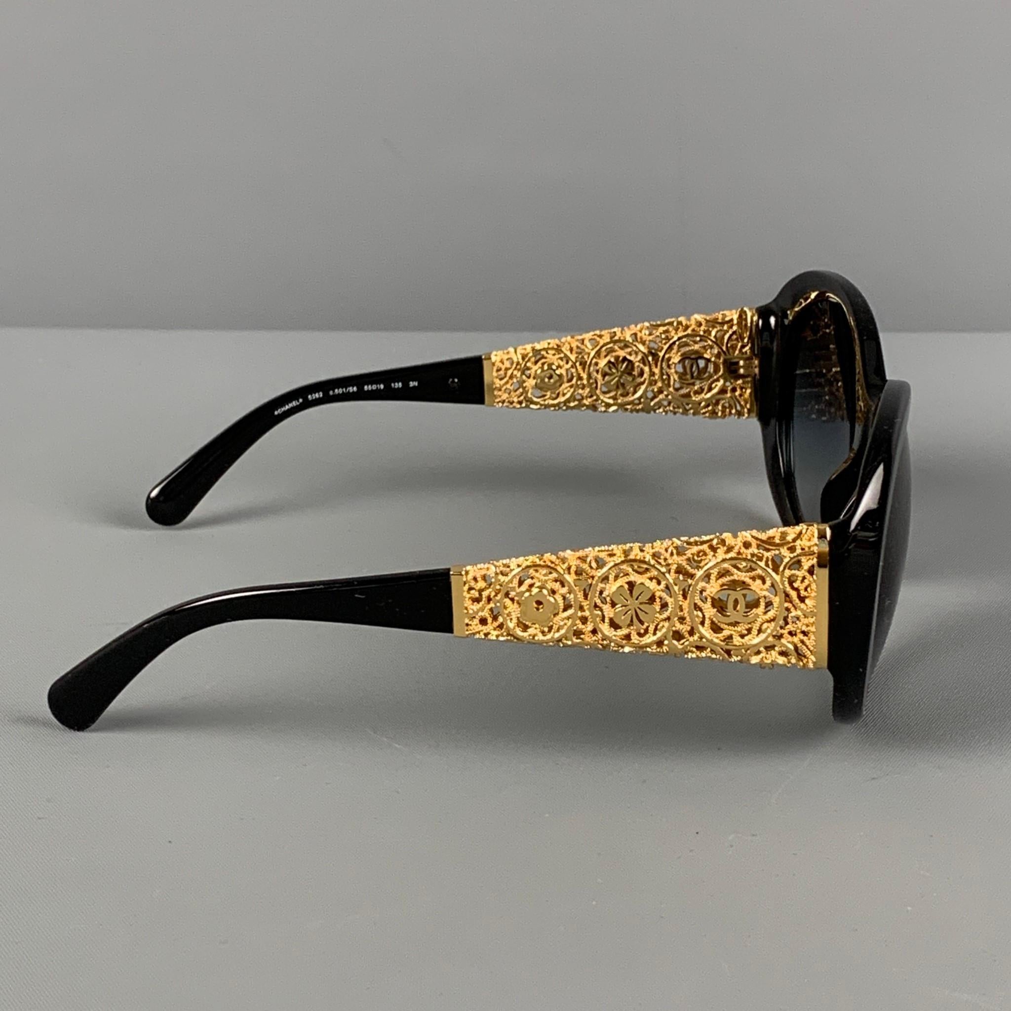 CHANEL 'Bijou' sunglasses comes in a black acetate featuring a metal crafted gold tone 'Camellia' floral motif design and a oval shaped tinted lenses. Includes case. Made in Italy. 

Very Good Pre-Owned Condition.
Marked: 5262 c.501/S6 55-19 135