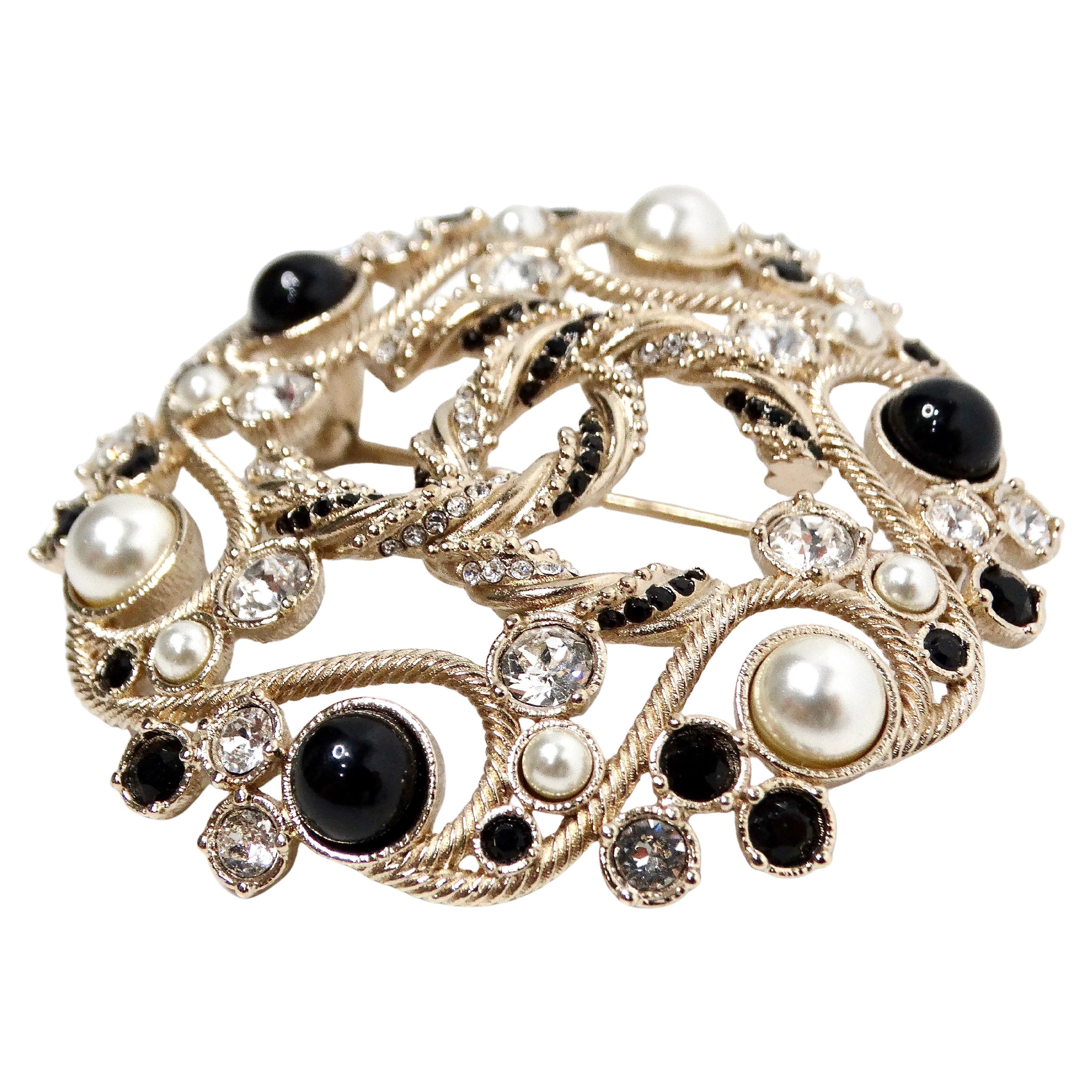 La spilla Chanel Black & Gold-Tone Costume Pearl Crystal Filigree del 2019 è uno splendido esempio della squisita artigianalità e dell'eleganza senza tempo del marchio. Caratterizzata dall'iconico logo CC intrecciato al centro, questa spilla emana