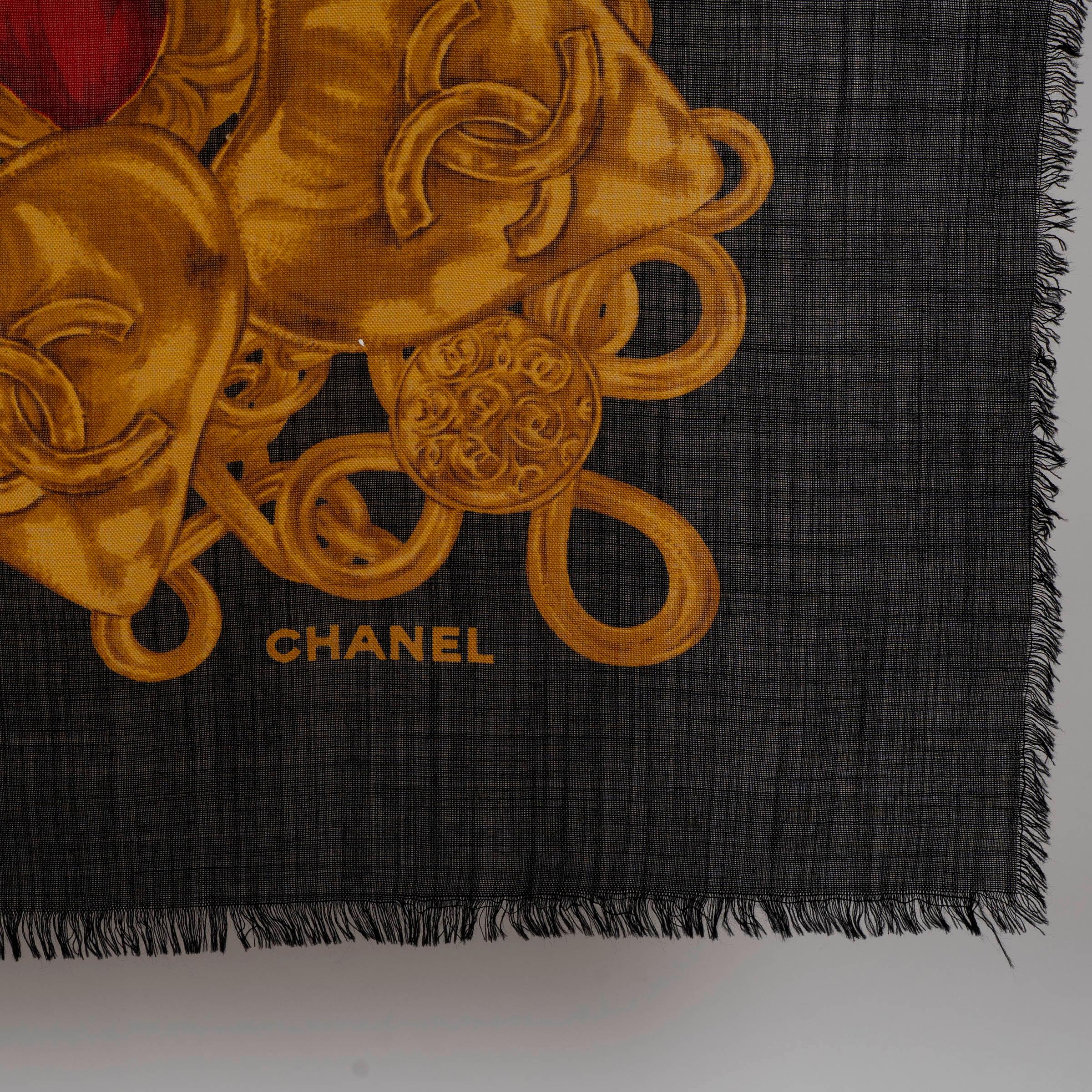 Questo scialle Chanel autentico al 100% è realizzato in lana nera (70%) e seta (30%), ornato da una sorprendente stampa ispirata ai gioielli in oro antico, rosso e verde. Il design è caratterizzato da catene decorate, medaglioni sovradimensionati e