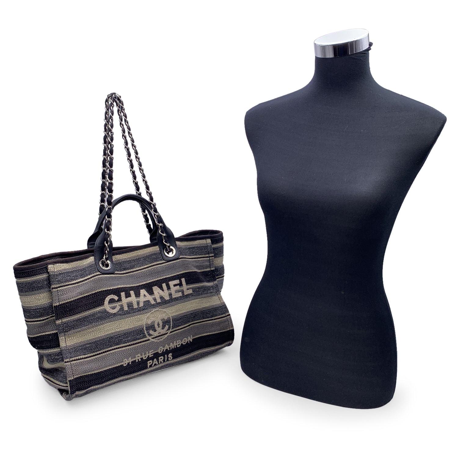 Beautiful Chanel 'Deauville' tote, crafted in black, grey and beige striped canvas with a white 'Chanel CC31, Rue cambon - Paris' logo. Period/Era: 2018/2019. Double black eather top handles and silver metal and interwoven leather shoulder straps.
