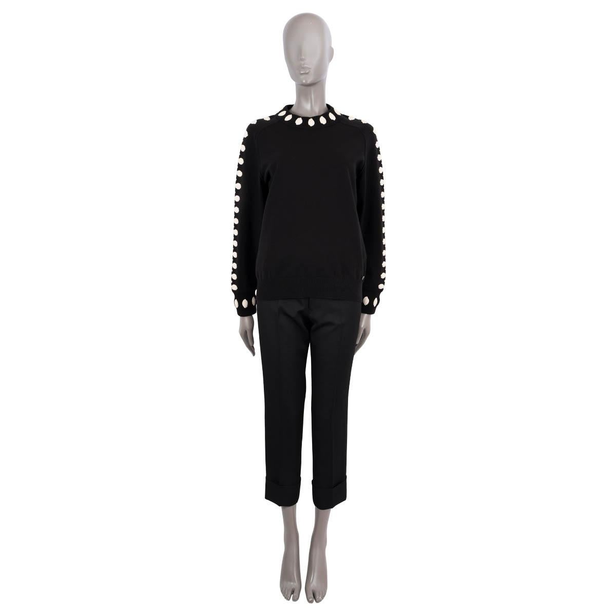 100% authentischer Chanel-Strickpullover aus schwarzer Wolle (76%), Polyester (18%) und Viskose (1%). Mit elfenbeinfarbenen Kamelienapplikationen, einem Logoknopf auf der Vorderseite und  Rippenbündchen. Unbeschriftet. Wurde getragen und ist in