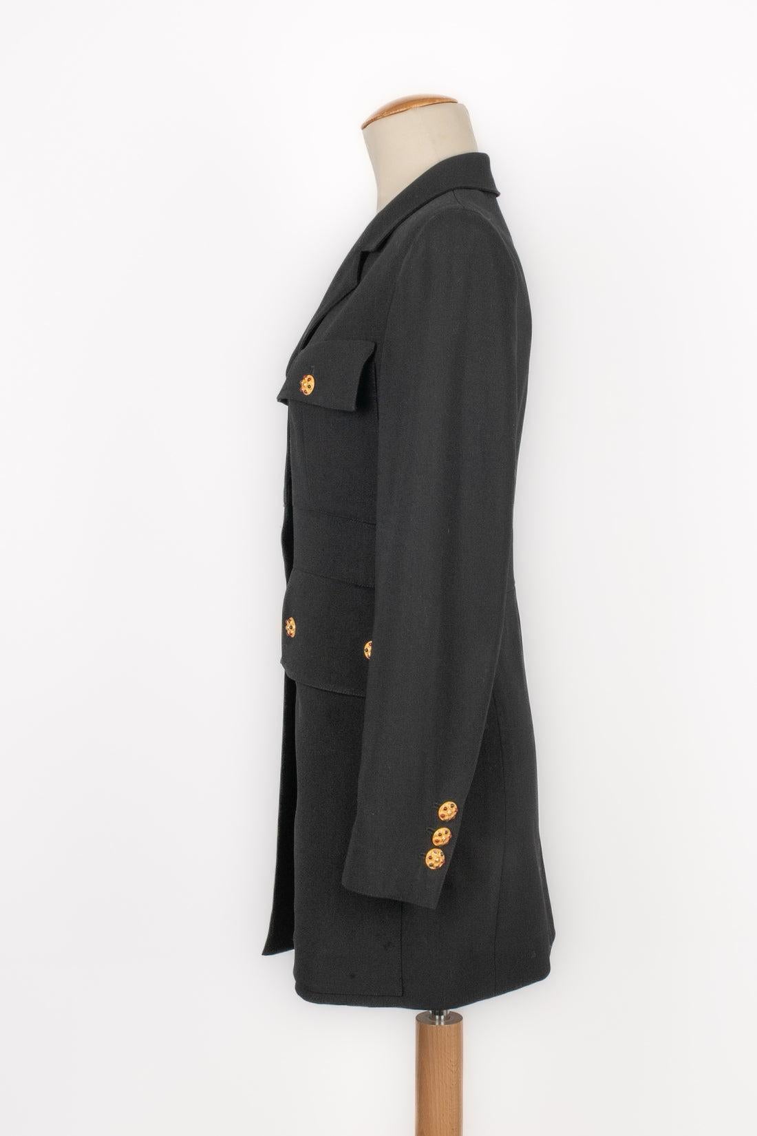Chanel - Mid-length black jacket decorated with golden metal and multicolored glass paste buttons. No size indicated, it fits a 36FR. Piece from the 1990s. To be mentioned, there is a slight worn marks on the sleeve cloth.

Additional