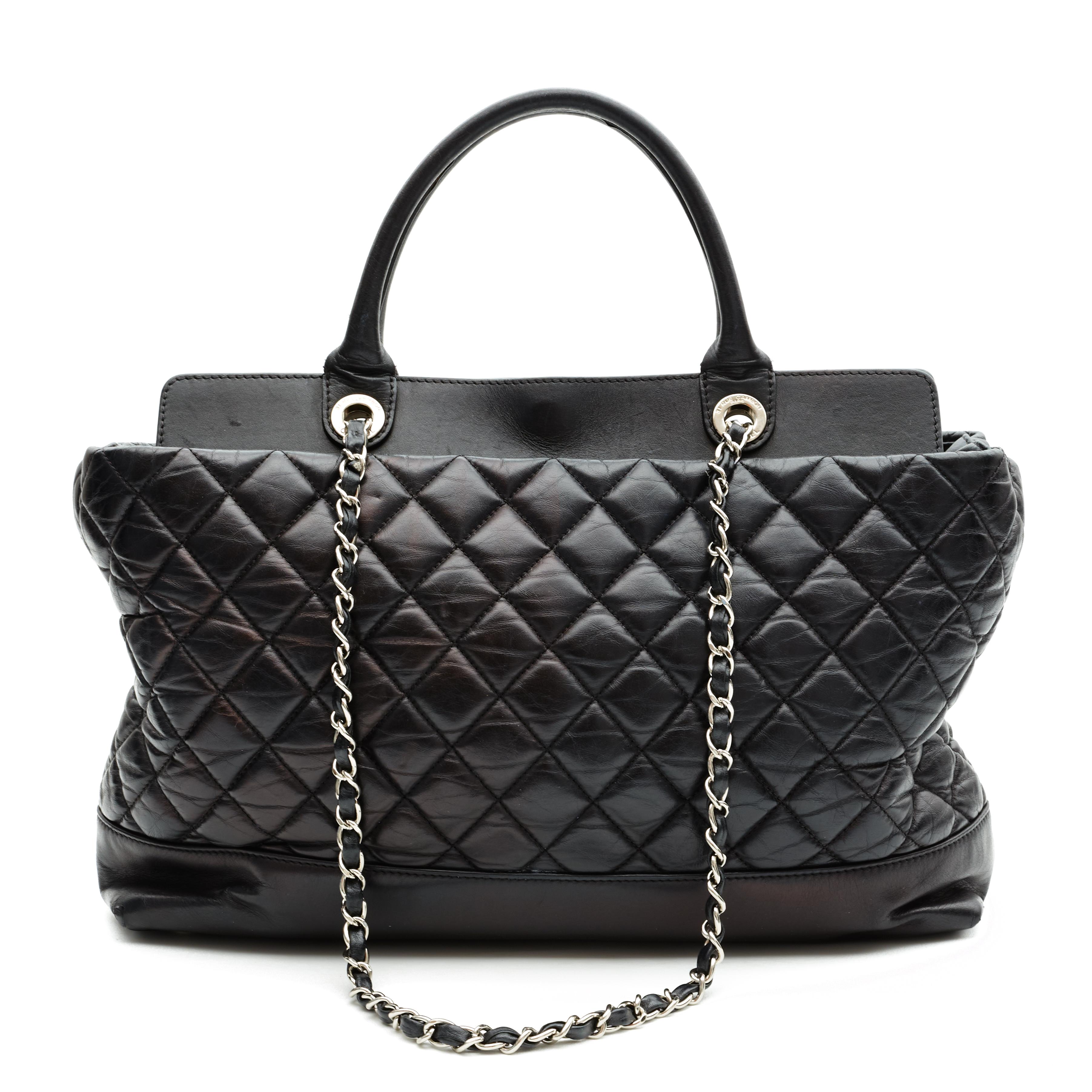 This Chanel shopping tote is made with black lambskin with diamond quilted stitching. The bag features dual rolled leather top handles, long shoulder chain interlaced with leather shoulder strap, CC turn lock closure, protective feet,  and a beige