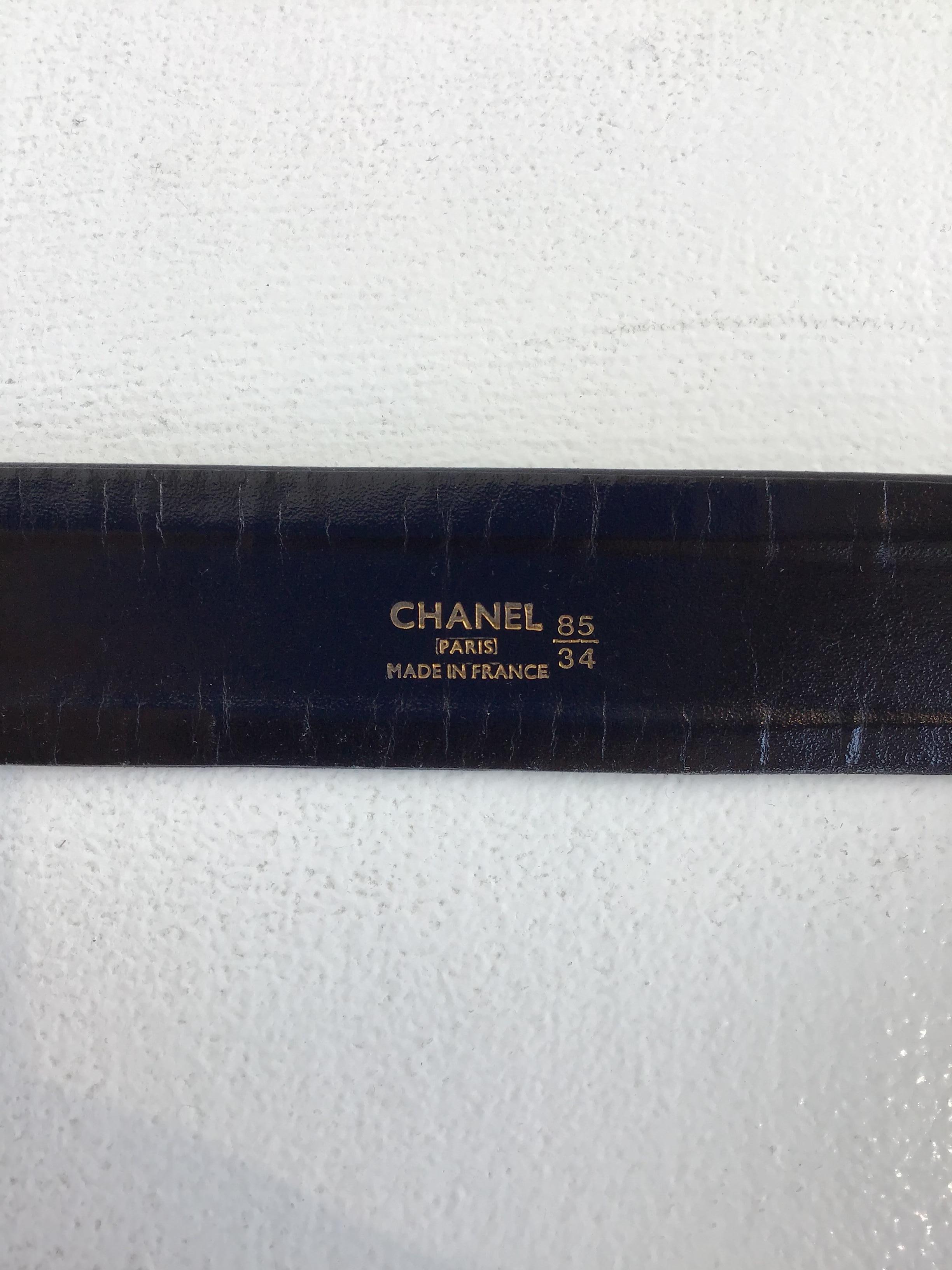 Chanel Black Leather Belt with Gold Chain. Featuring a thick leather strap with gold tone square metal buckle that reads CHANEL. Chain includes signature coin charm. Made in France. Size 34.