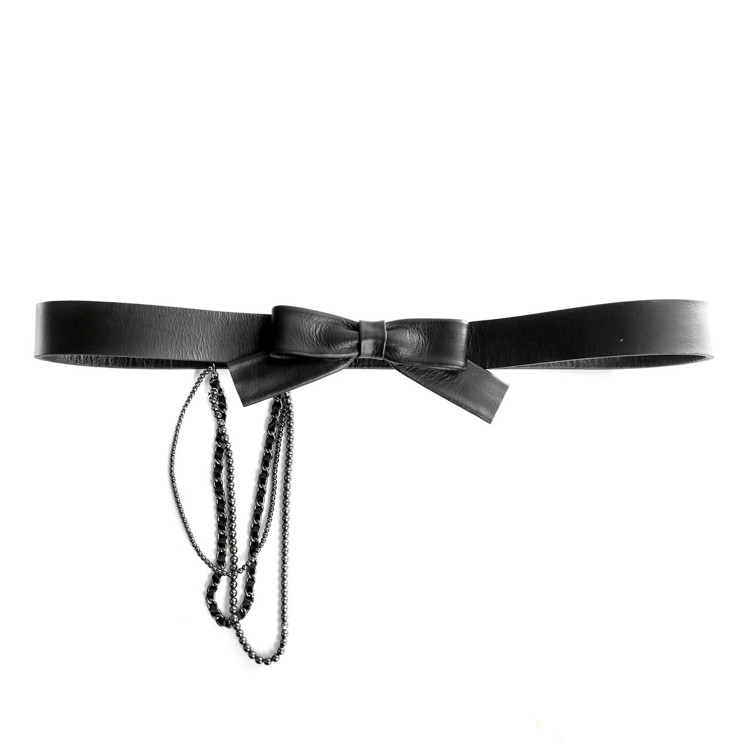 This authentic Chanel Black Bow Belt is in mint condition.  Black leather belt is covered with black wool fabric and has a central bow closure.  Three different style chains dangle decoratively from the side.  Snap closure.   Made in France. Size