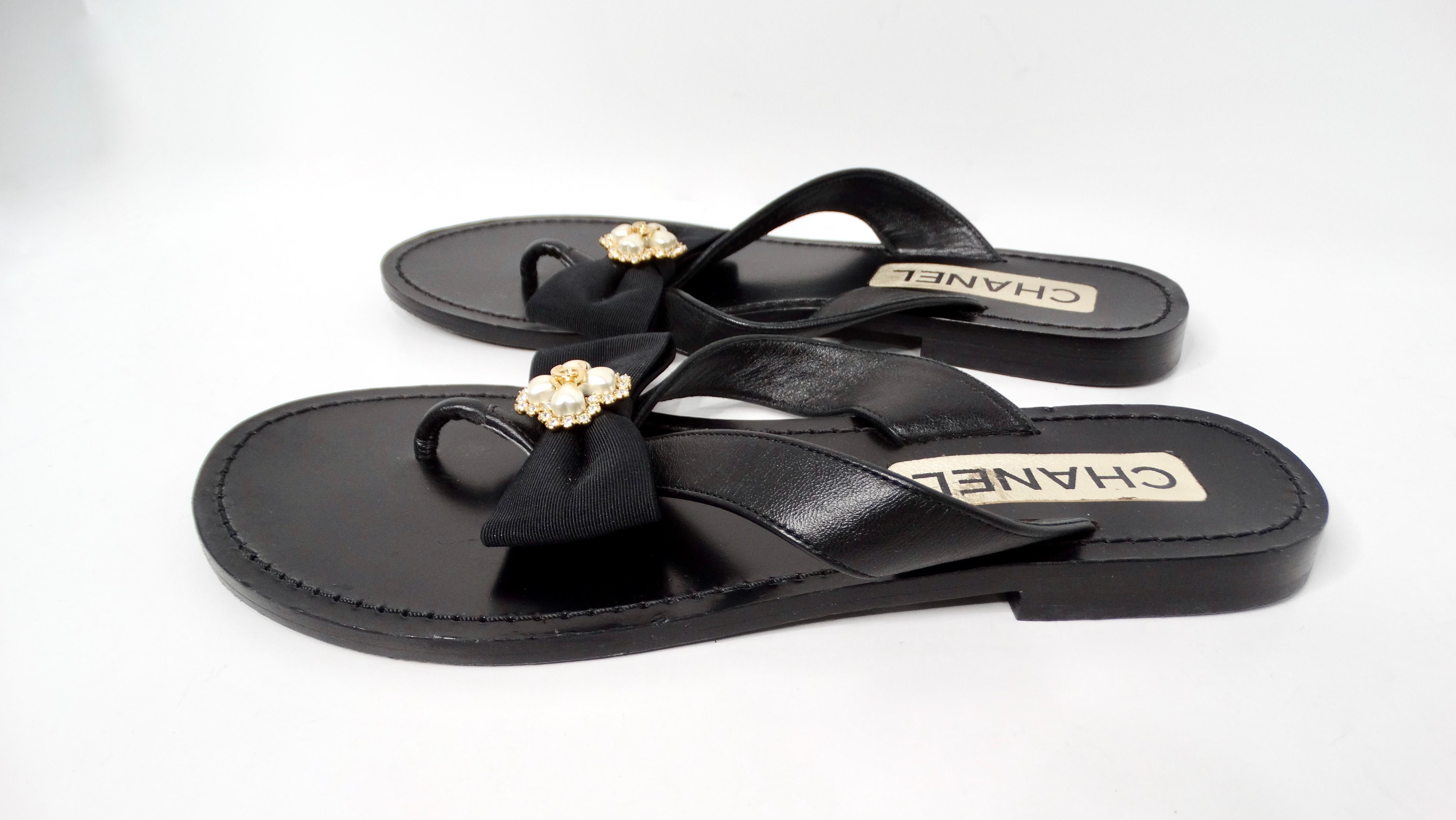 Elevate your summer wardrobe with the exquisite Chanel Black Leather Bow & Pearl Accent Sandals. These luxurious thong sandals feature a striking black leather design that effortlessly blends elegance and comfort. The standout element is the