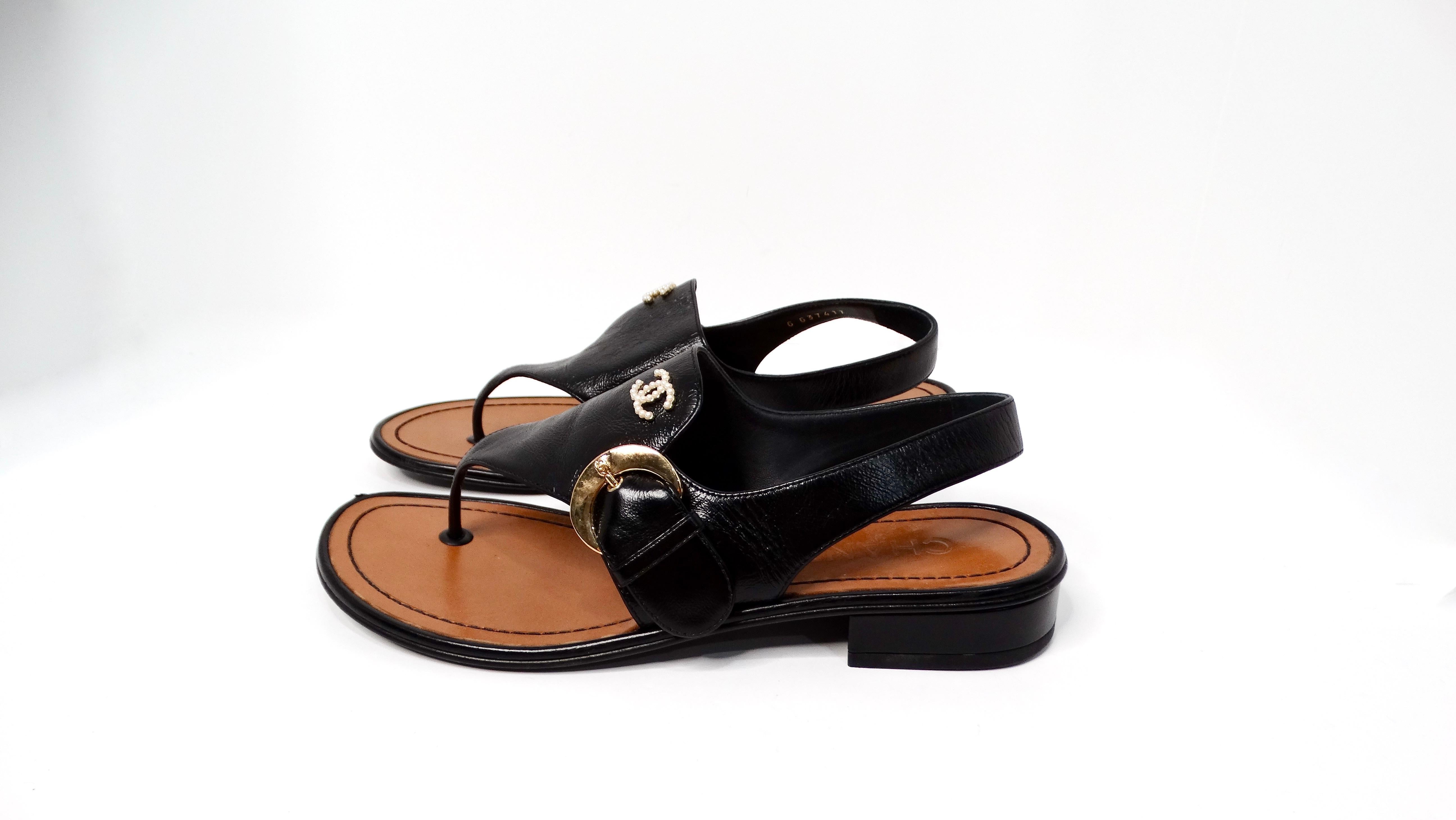 The Chanel Black Leather Buckle Sandals with Pearl Interlocking CC Logo are an elegant blend of modern sophistication and timeless design. Crafted from luxurious shiny black leather, these sandals boast a sturdy brown leather base that adds depth