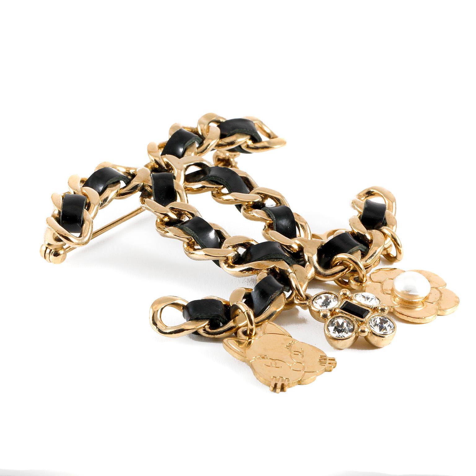 This authentic Chanel Black Leather CC Charm Brooch is in pristine condition.  Interwoven black leather and gold chain large interlocking CC pin with four iconic Chanel charms.  Cats, clovers and camellias adorn this stunning brooch.  Pouch or box