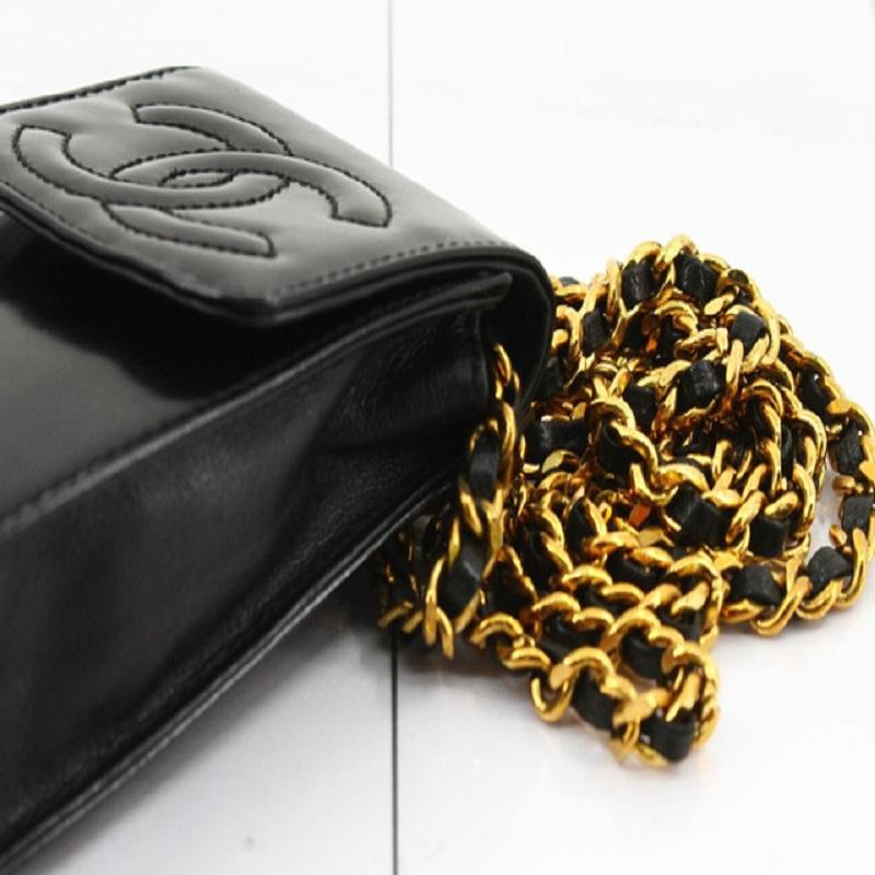 Black leather Chanel CC Stitch Phone Holder crossbody bag with gold-tone hardware, interlocking CC logo stitched at front, woven leather and chain-link shoulder strap, front flap with stud closure that will open to black canvas