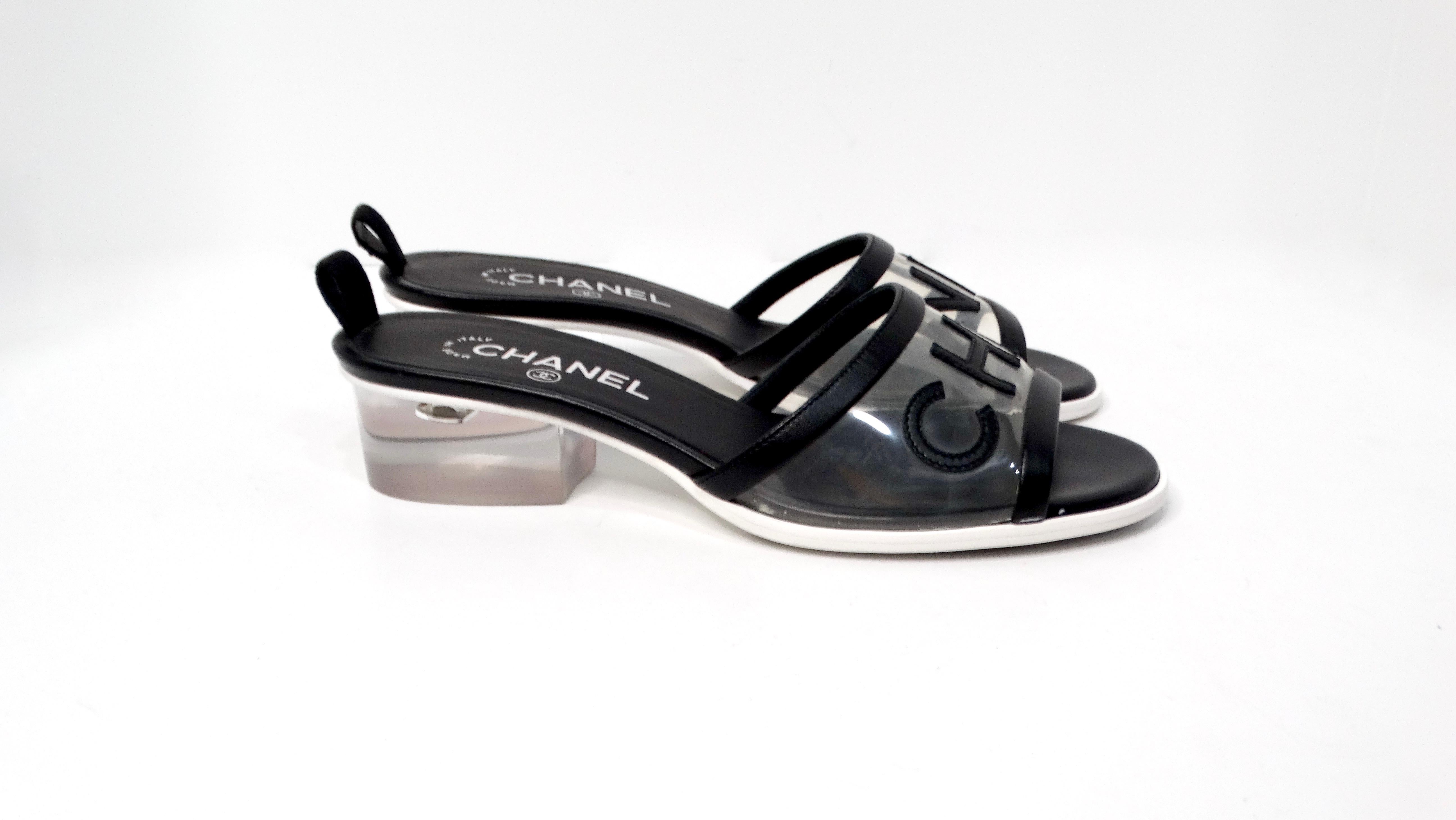 Step into luxury with the Chanel Black Leather & PVC Slide Sandals, featuring a striking design that effortlessly blends comfort and high fashion. Crafted from sumptuous black leather, these sandals showcase a sleek slide strap constructed from