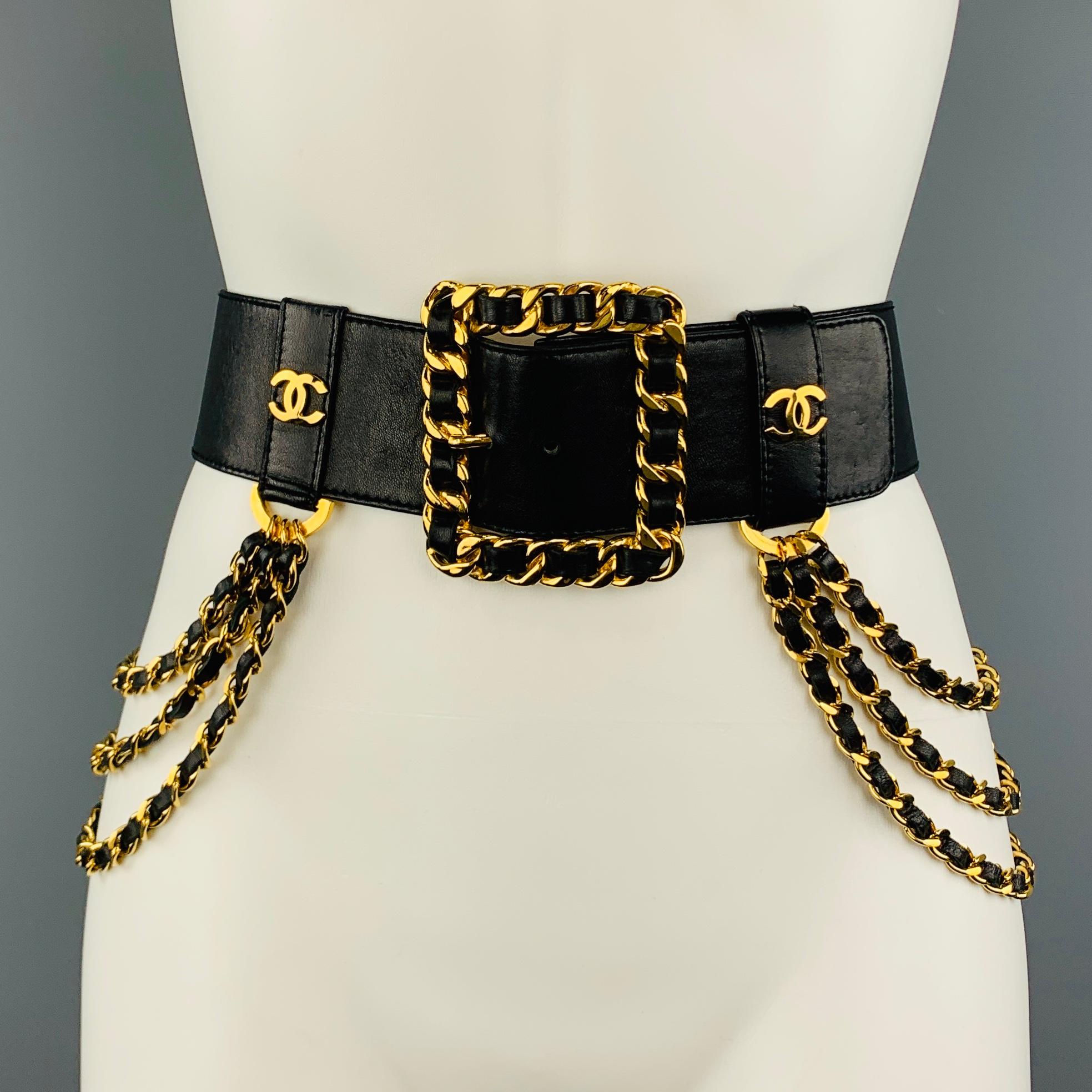 Vintage CHANEL Season 26 circa 1980's waist belt features a thick black leather strap with yellow gold tone leather woven curb chain square buckle, CC logo stud belt loops, and cascading triple drop chain side adornments. Made in France.
 
Excellent