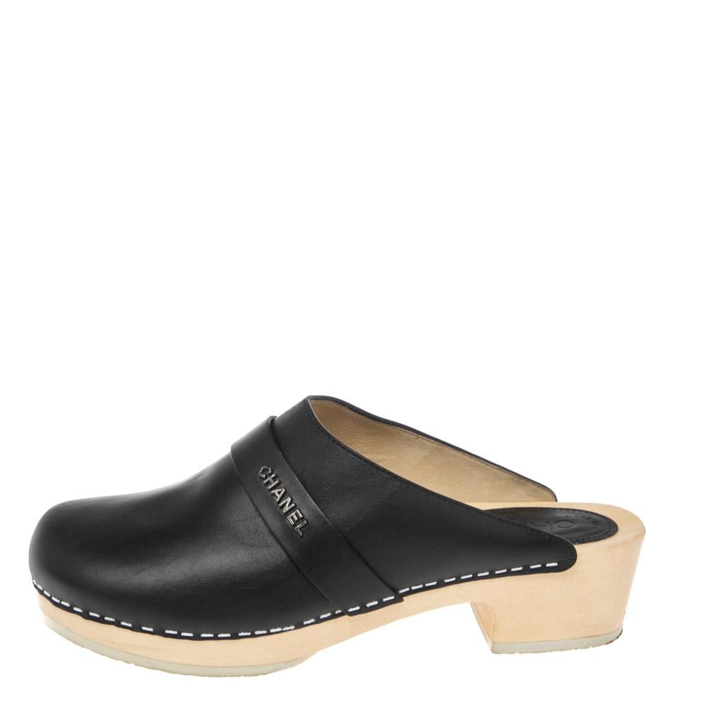 Vuoi qualcosa da abbinare al tuo abbigliamento casual? Questi zoccoli in legno con tomaia in pelle nera sono disponibili per te da Chanel. Infila questi tacchi a blocco che si chiudono sul davanti; il design della cintura incrociata al centro