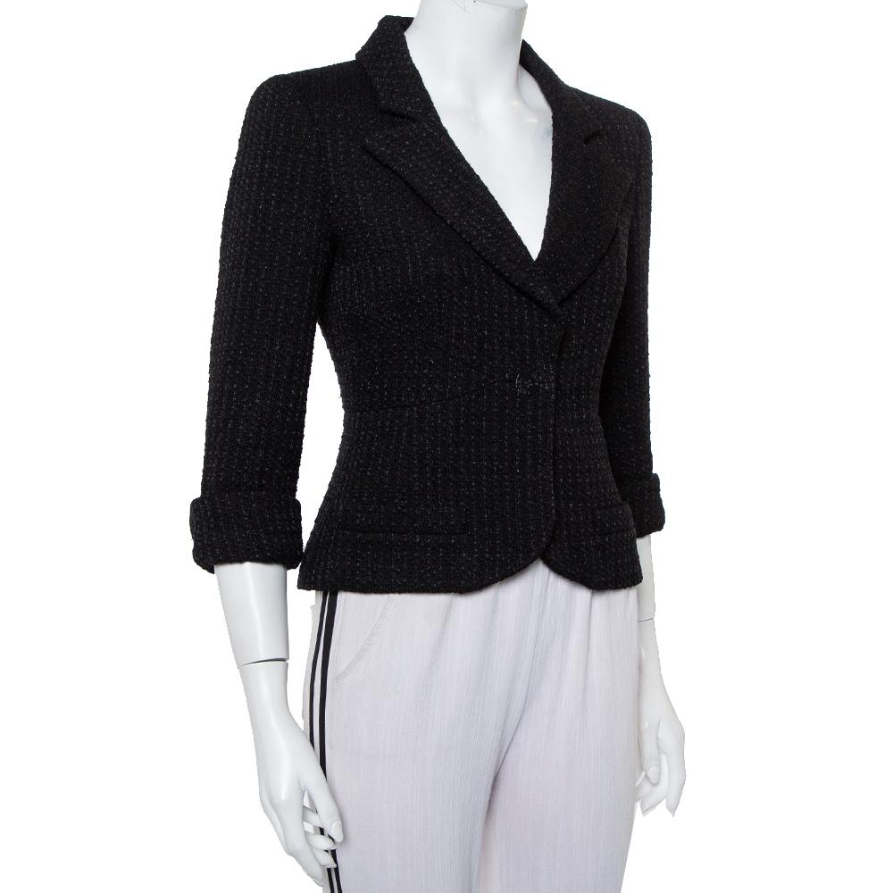 Chanel presents this exclusively designed contemporary blazer for the modern woman. The black tweed creation features a flattering silhouette with notched lapels, logo detailed button closure, and three-fourth sleeves. It will surely lend you a