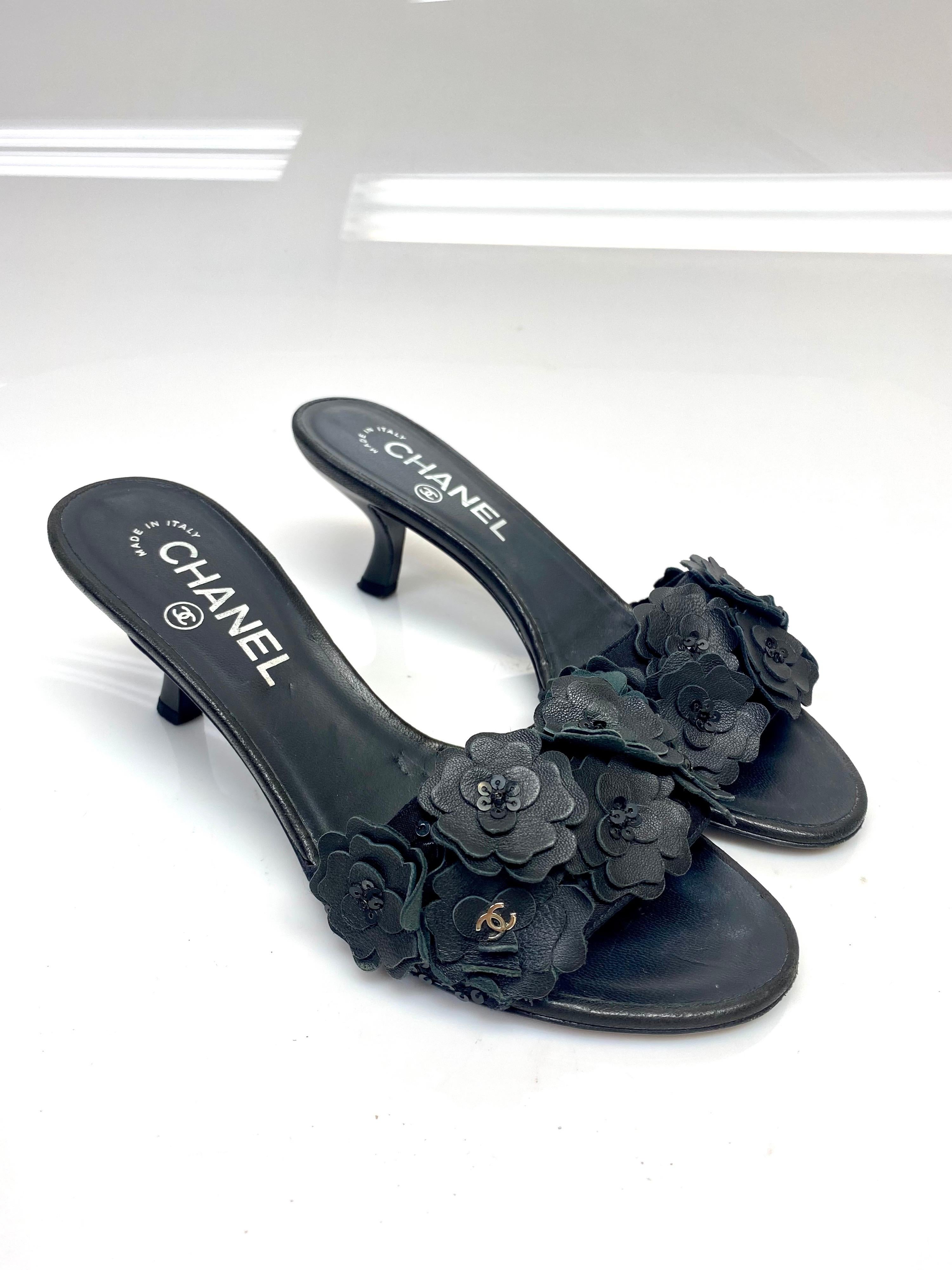 Chanel Black Multi Camelia Slides with sequin.  Size 35.5. These heeled slides from Chanel will bring you effortless style. They have been crafted from leather and designed with the brands signature Camellia's perched around the front of the shoe.