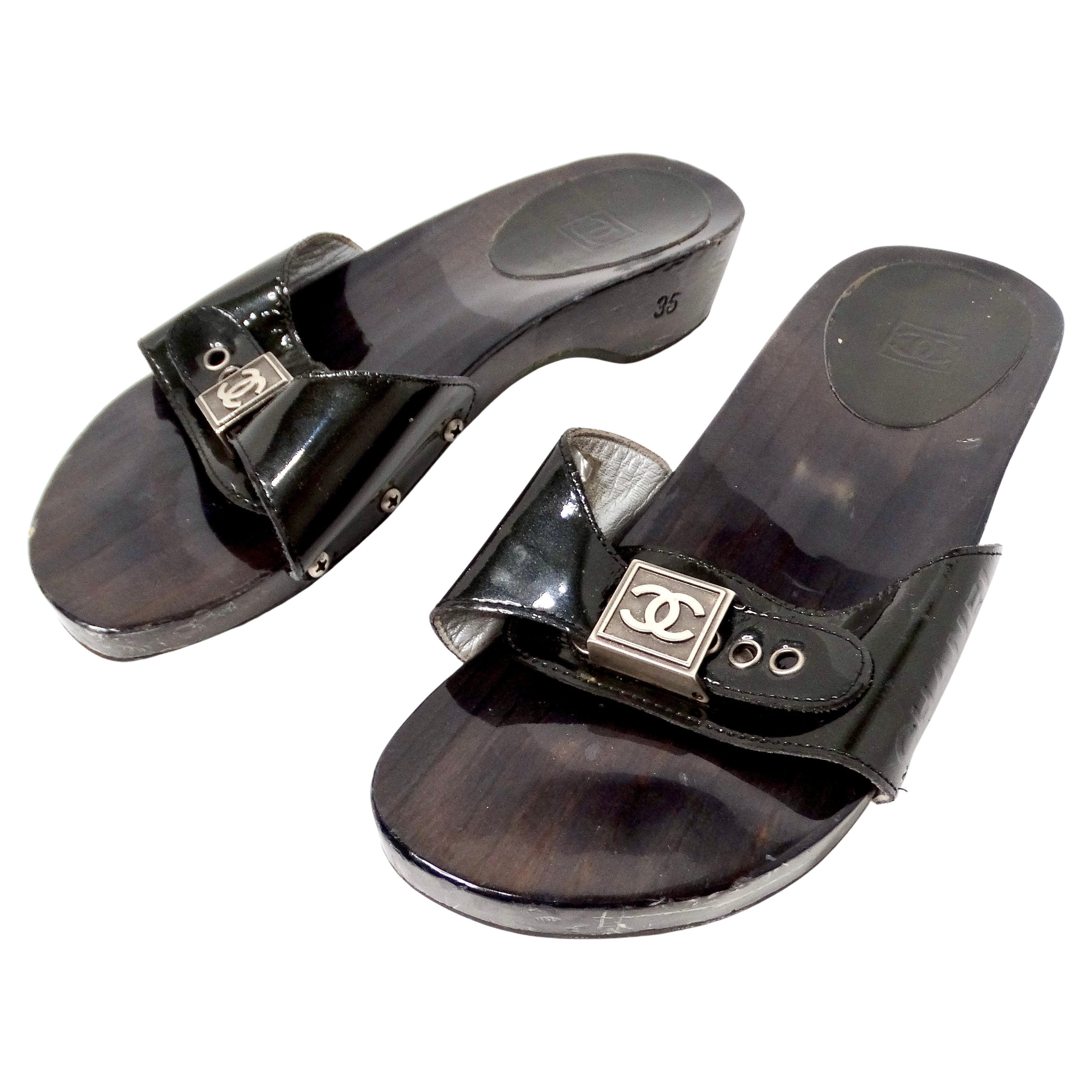 The Chanel Black Patent Leather & Wood Clog Slides circa Y2K are a striking example of early 2000s luxury footwear. Featuring a glossy patent black leather strap that gracefully arches over the toes, the design is accentuated by an iconic