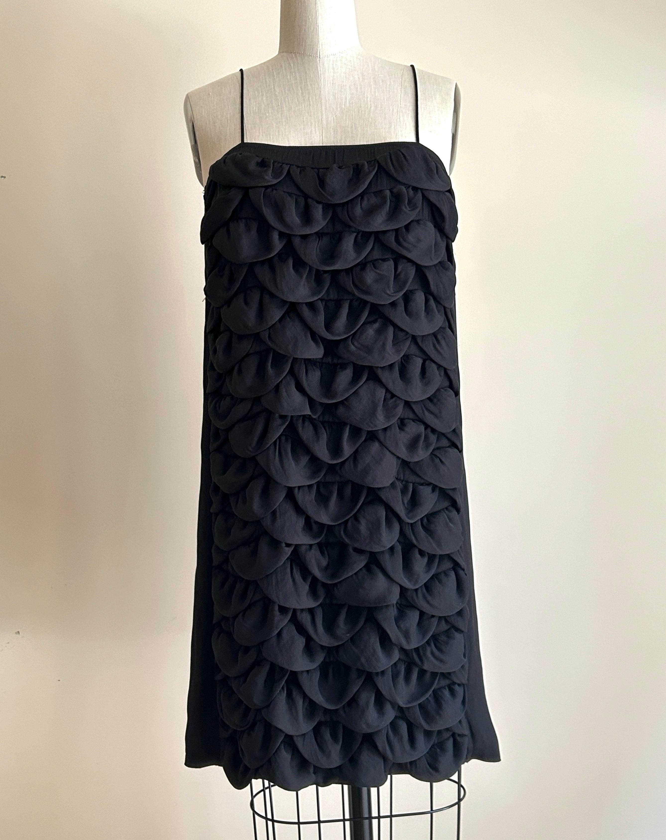 Schwarzes ärmelloses Chanel-Kleid im Vintage-Stil aus den 2000er Jahren mit blütenförmigen Stoffbahnen vorne. Aus der Kollektion Cruise 2009. CC-Logo aus Metall oben auf der Rückseite. 

Leichtes Material, ideal zum Überziehen am Strand oder am Pool