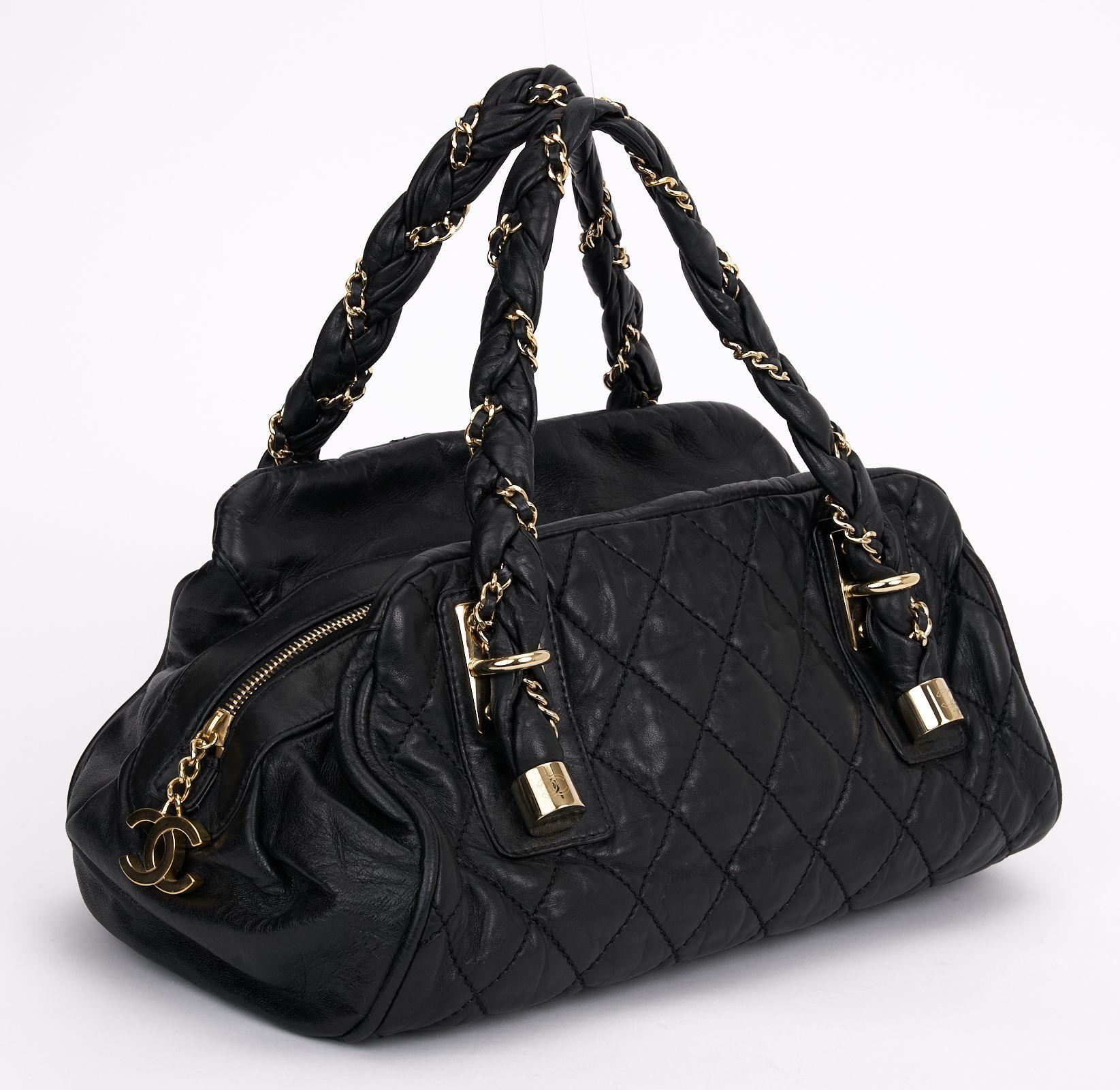 This Chanel Lady Braid Bowler Bag Quilted Distressed Lambskin from black quilted leather,  features intertwined leather and gold chain straps, protective base studs, CC logo hardware, and gold-tone hardware accents. Its top zip closure opens to a