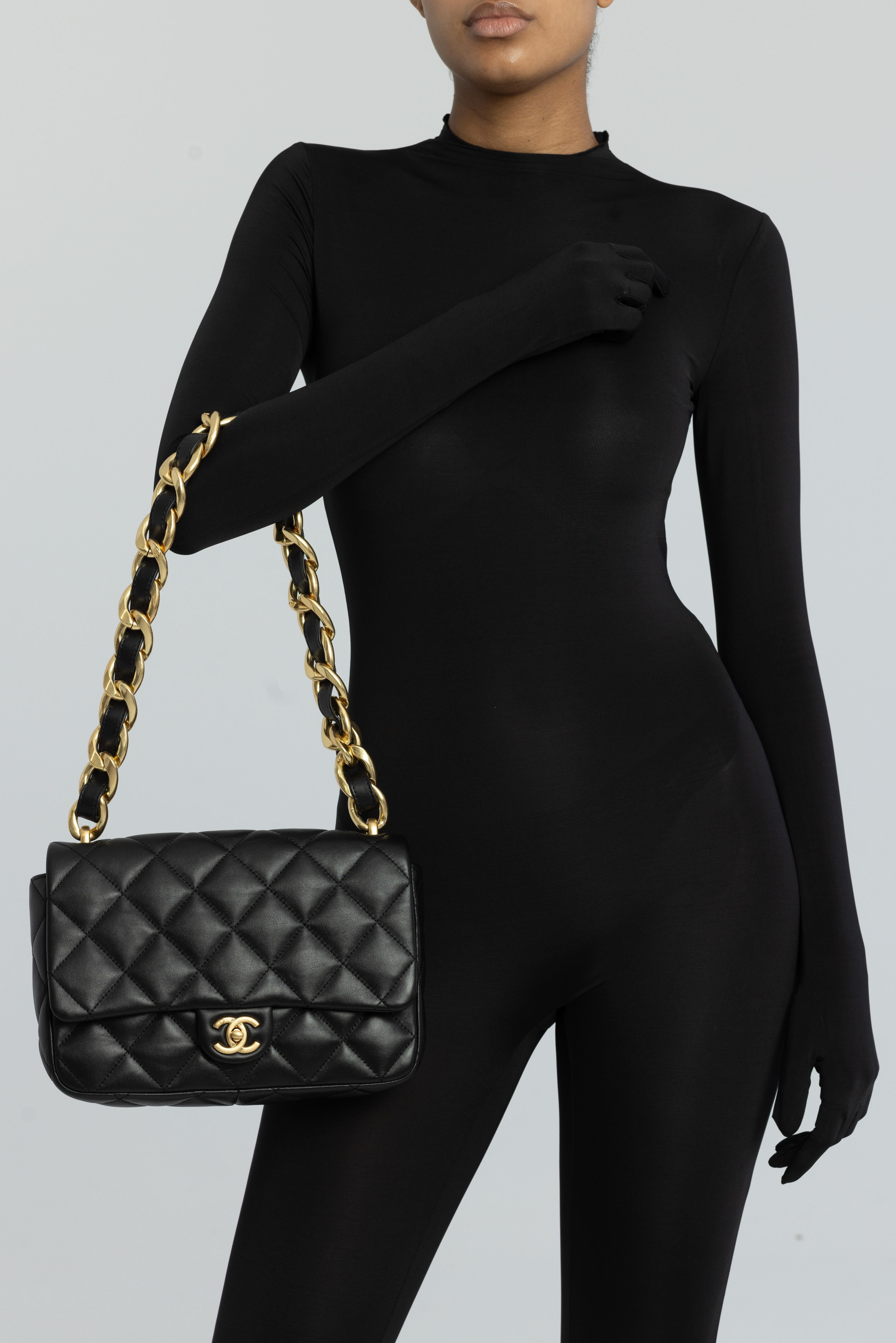 Este bolso de hombro clásico de Chanel está fabricado en piel de cordero acolchada, suave y flexible, en color negro. Lleva una bandolera de eslabones de cadena dorada de gran tamaño enhebrada con cuero y un cierre giratorio CC clásico dorado. El