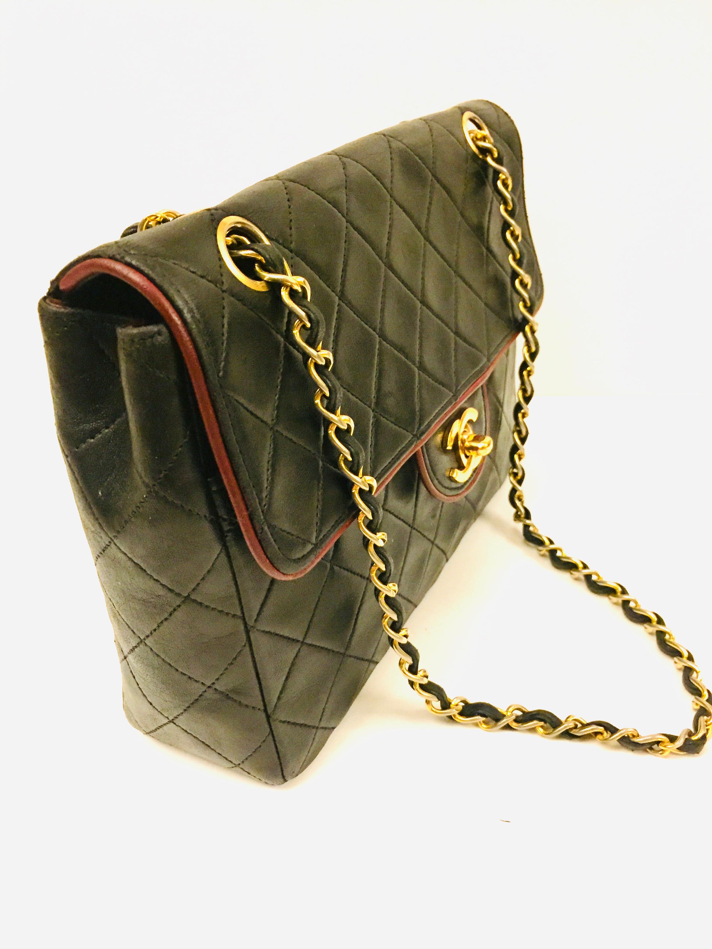 - VIntage 80s Chanel black quilted lambskin with red piping gold chain shoulder bag. 

- Red interior leather with compartments and zip closure. 

- Turn lock closure. 

- Back pocket. 

- Sticker, dust bag.

- Measurements: 24cm x 15cm x 6cm.