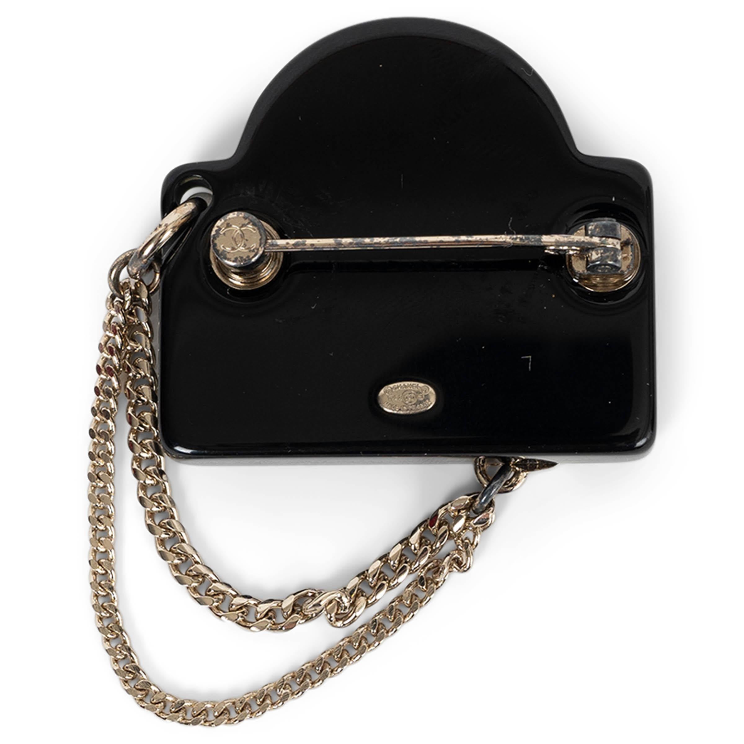 This 100% authentic Chanel street sign brooch in black resin is a bold and playful statement piece. Accented with gold-tone details, it features three pearly white resin pearls, a strass-encrusted signature, and a classic CC logo. Two delicate