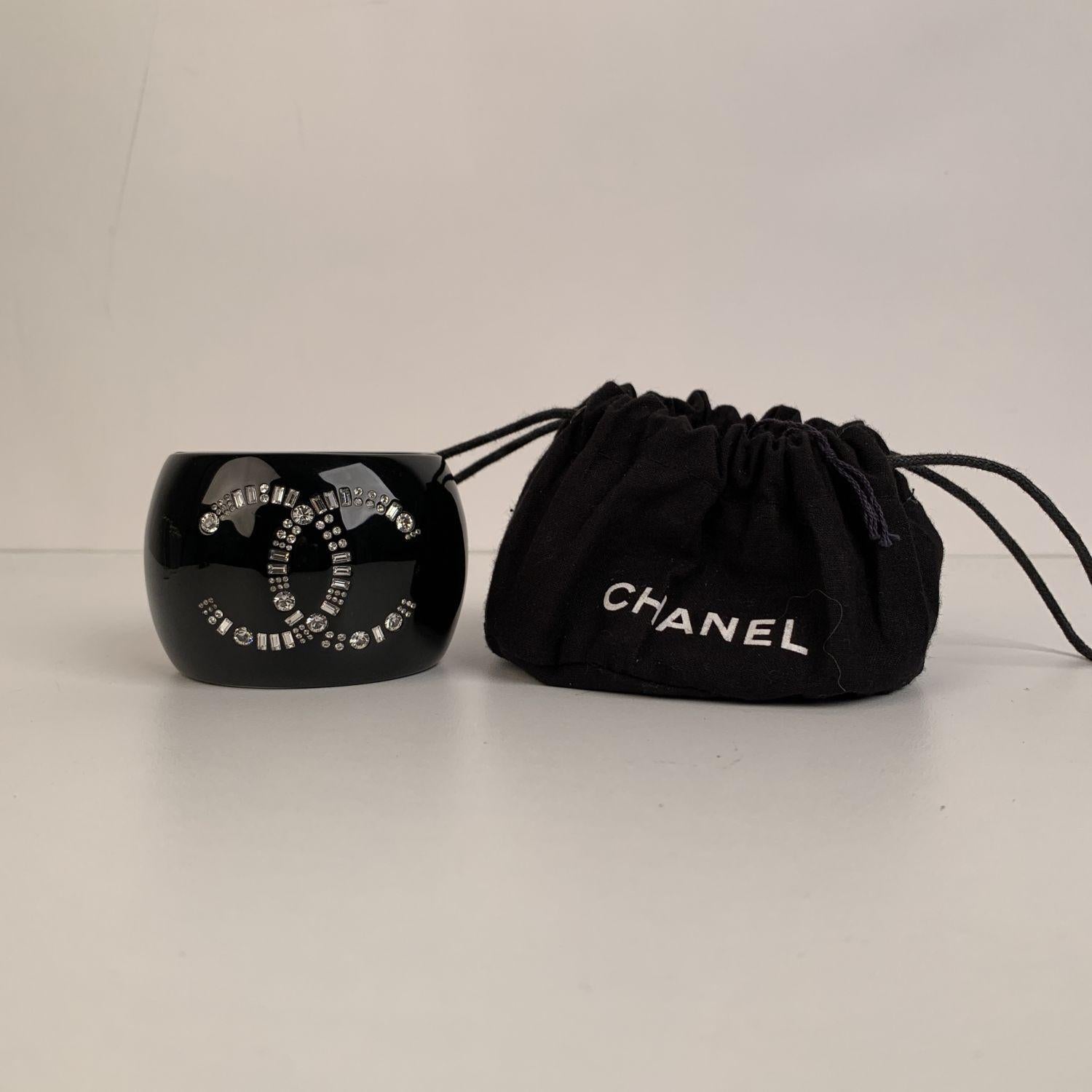 Lovely large cuff bracelet by CHANEL. Black resin with crystal CC logo at center. Hinge opening with magnetic clasp closure Stamped 'Chanel 09 CC A Made in France' internally. Height: 2.25 inches - 5,7 cm. Will fit up to approx. 6.5 inches - 16.5 cm