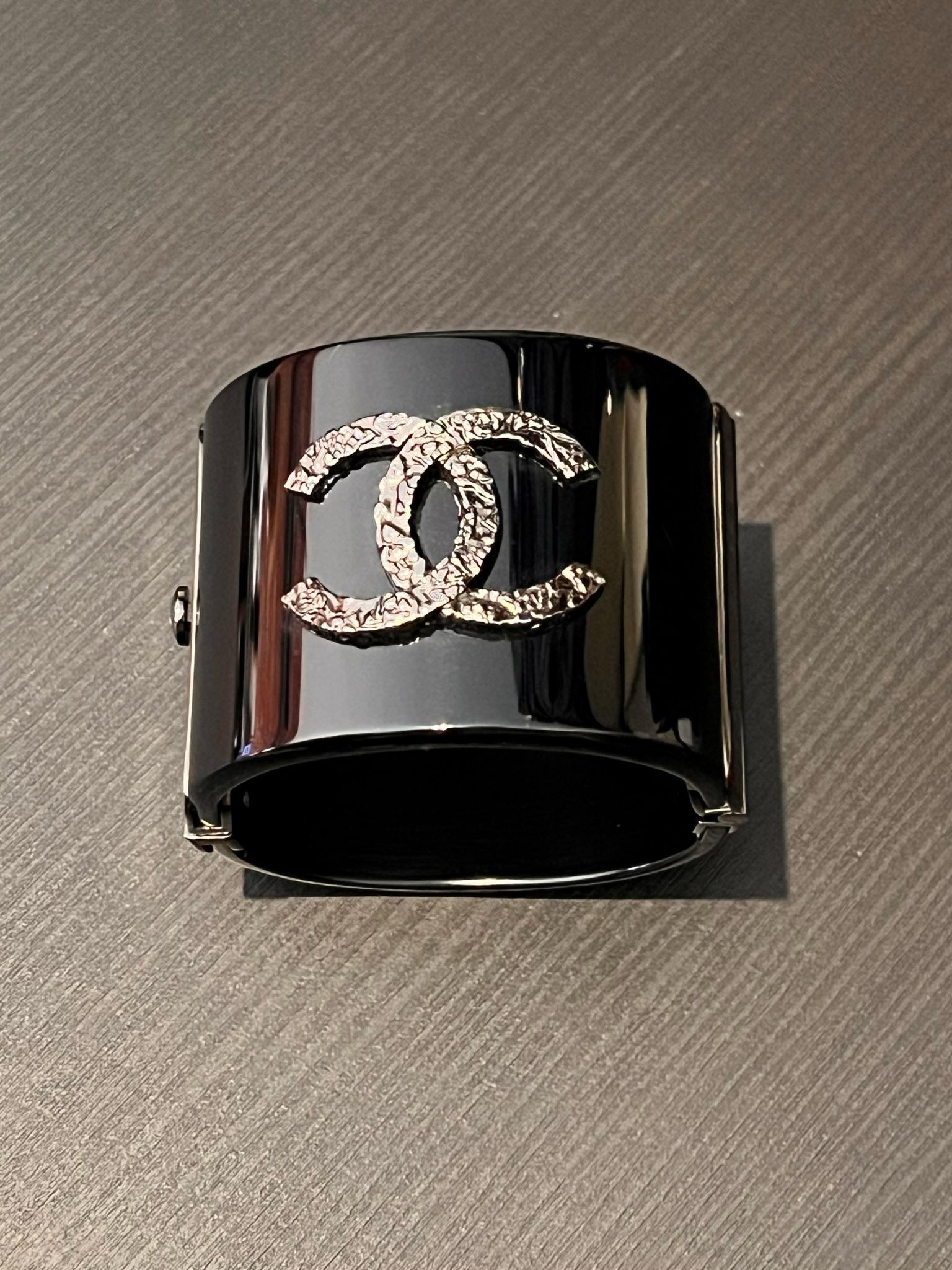 This is an authentic CHANEL Resin CC Cuff Bracelet in Black and silver. This bold and elaborate cuff is crafted of black resin. The cuff is accented with a classic CC logo in textured silver and opens with a matching silver button clasp. This is a