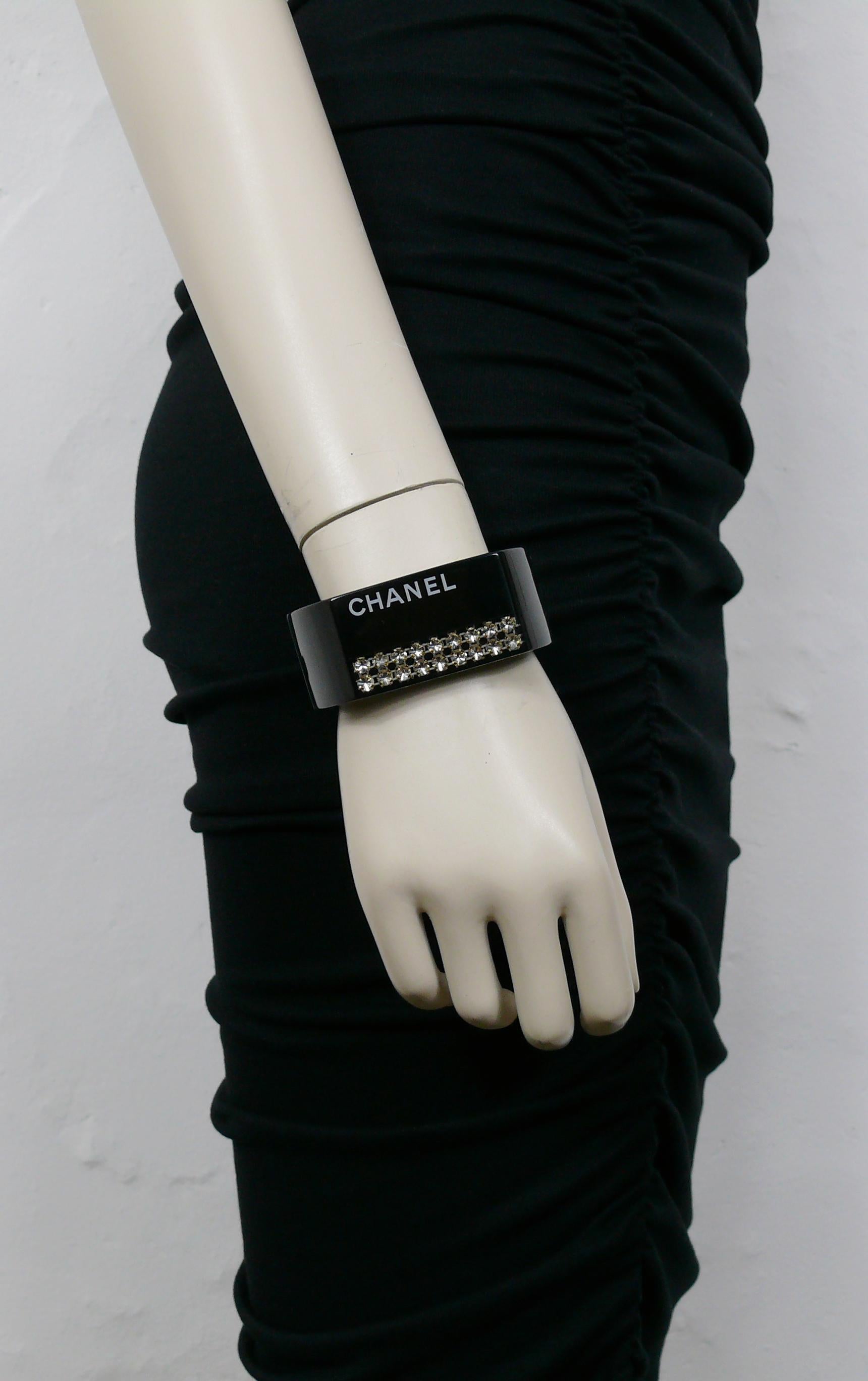 CHANEL black resin clamper cuff bracelet featuring a white CHANEL logo and two clear crystal chains inlaid.

Spring 2005 Collection.

Magnetic closure.

Embossed CHANEL 05 P Made in France.

Indicative measurements : inner approx. 5.7 cm (2.24
