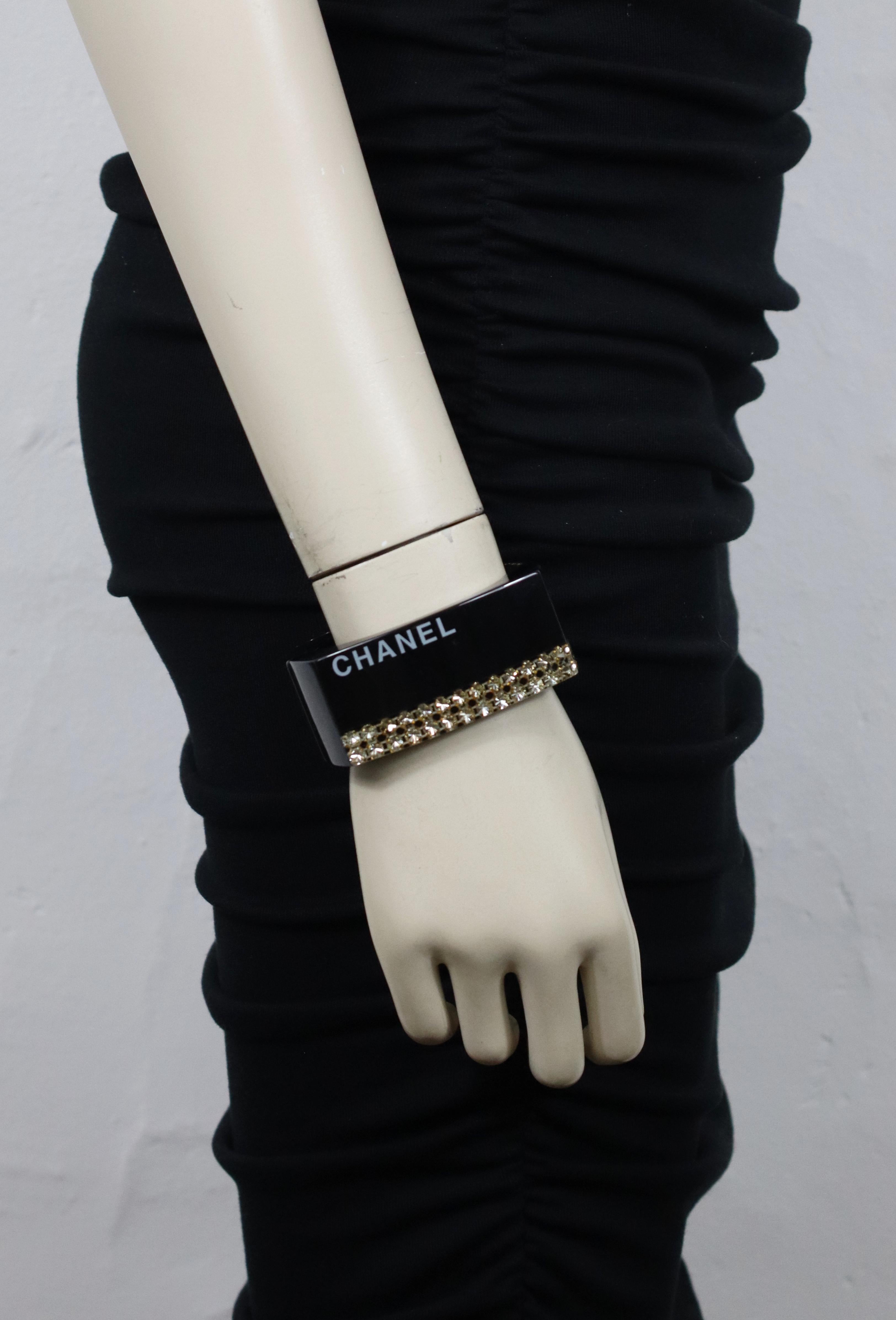 CHANEL black resin clamper cuff bracelet featuring a white CHANEL logo and two clear crystal chains inlaid.

Spring 2005 Collection.

Magnetic closure.

Embossed CHANEL 05 P Made in France.

Indicative measurements : inner approx. 5.7 cm (2.24