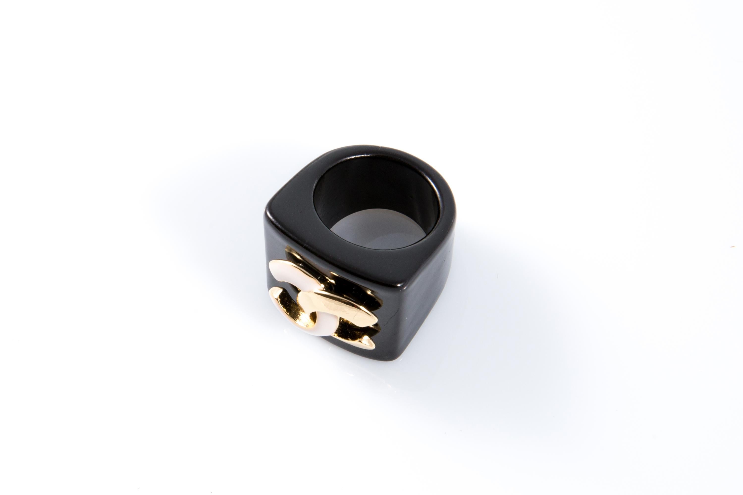 Chanel Black resin large knight ring featuring  a white and gold-tone signature interlocking “CC”, signature a plaque inside.  
Estimated size: 54
Circa 2000s . 
Good vintage condition. Made in France.  
Front Width: 1in (2.5cm)
Please note this