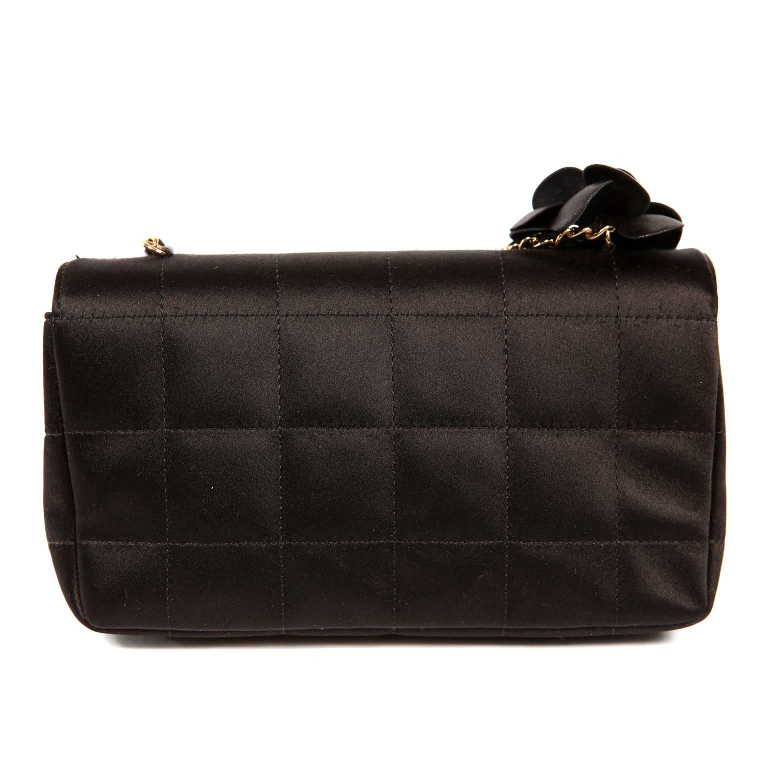 Chanel - Sac à bandoulière Camellia en satin noir - état impeccable
 Elegant et intemporel, ce sac de soirée chic s'ajoute intelligemment à toute collection. 
Le petit sac à rabat en satin noir est piqué d'un motif carré.  Une fleur de camélia en