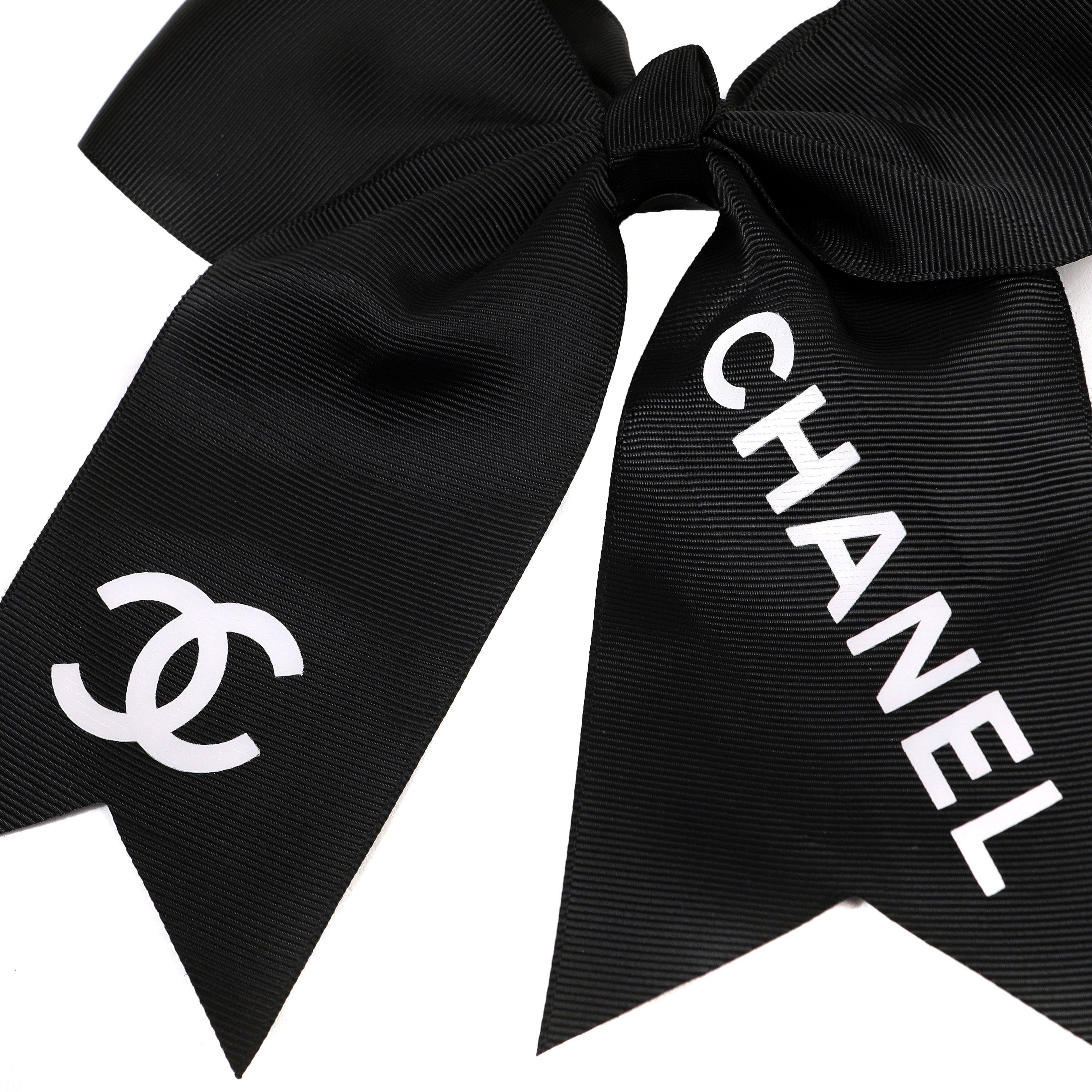 This authentic. Chanel Black Cheer Bow Hair Tie is pristine.  Oversized black grosgrain bow with white CC and CHANEL lettering.  Elastic tie attached.  
PBF 13940

