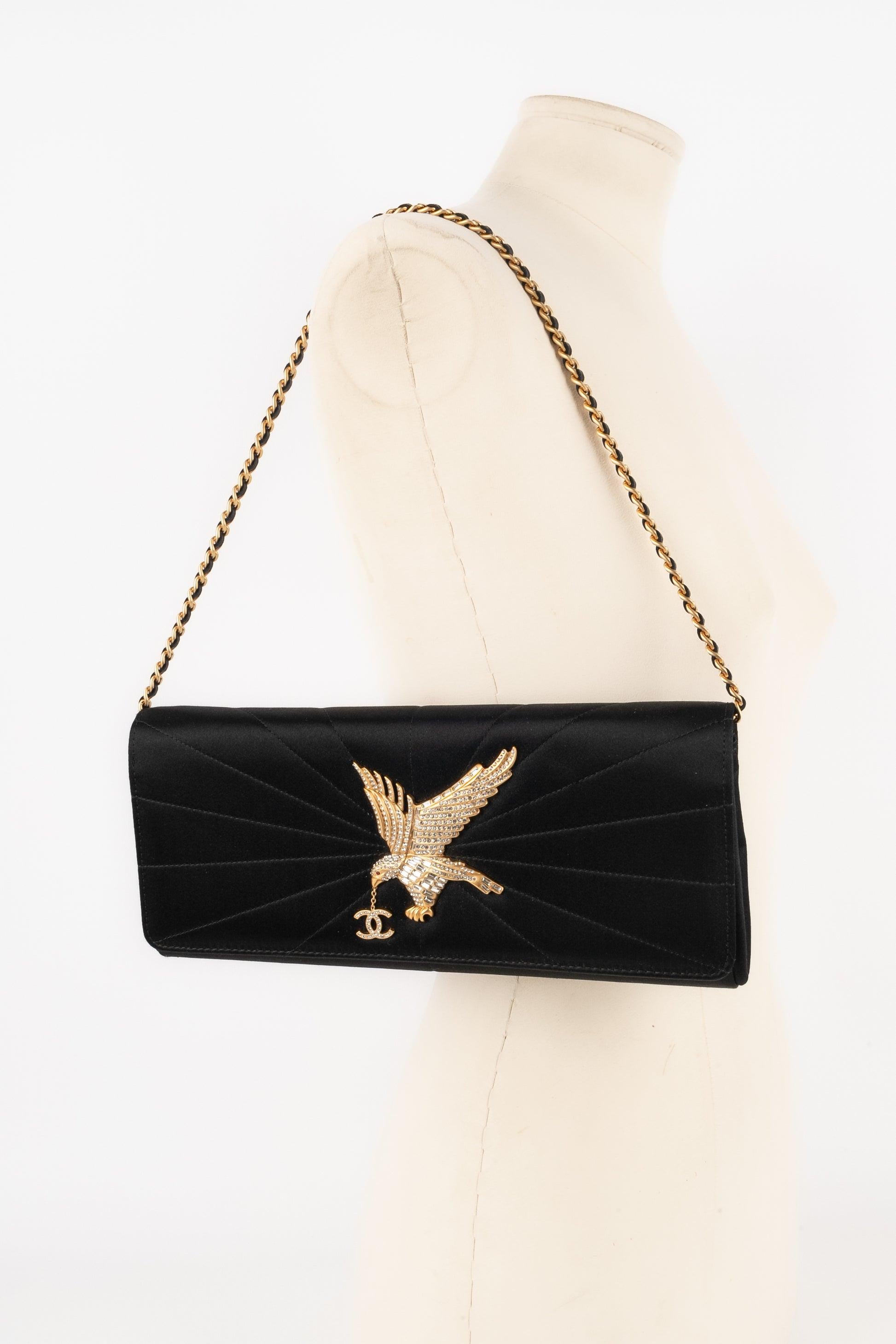 Chanel - (Made in Italy) Black satin clutch bag with radiant topstitches topped with a golden metal eagle pattern ornamented with rhinestones. Black leather inside and golden metal crossbody chains interlaced with leather. 2001 Spring-Summer