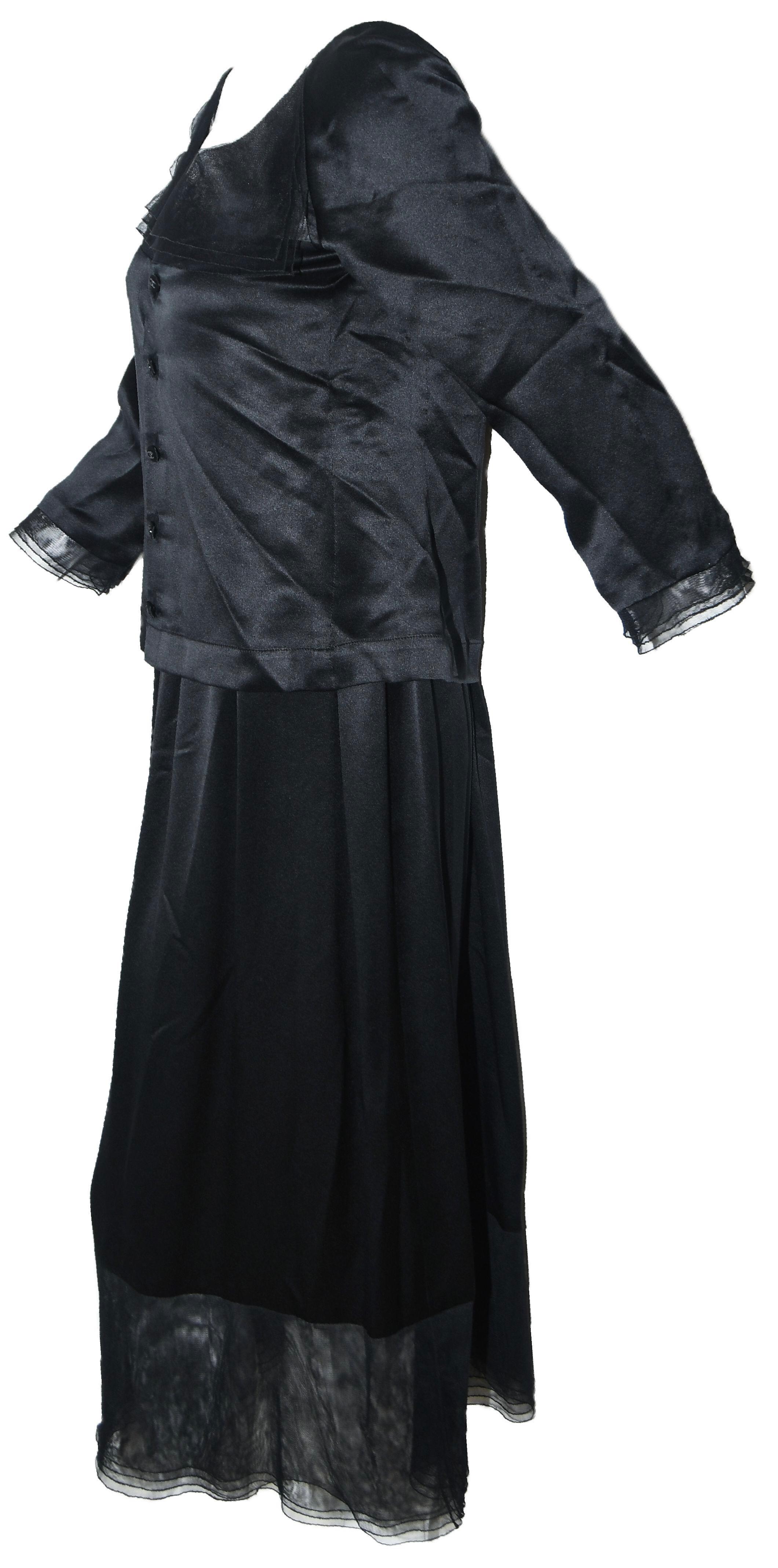 Chanel black silk two piece dress is composed of a 3/4 sleeve blouse contains 5 Chanel CC buttons at back for closure with mesh band across collar bone and sleeves finishing with lace ruffle.  The long skirt is gathered at waist and includes 4 black