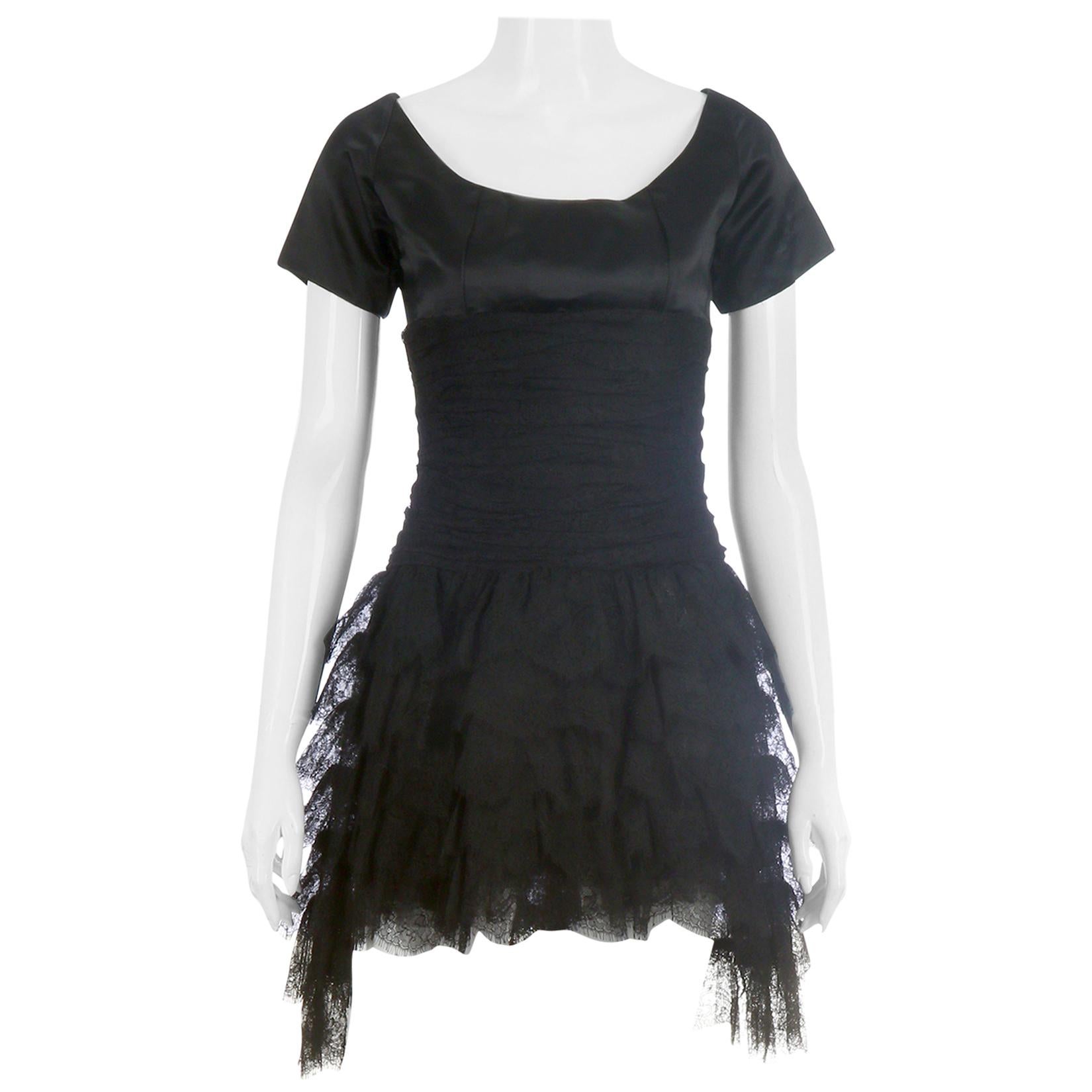1980's Chanel black short-sleeved mini dress comprised of a medium weight silk fitted upper bodice, a horizontally ruched lace mid-section, a fitted waist made of gathered lace and a multi-tiered lace skirt. The dress fastens down center back by a