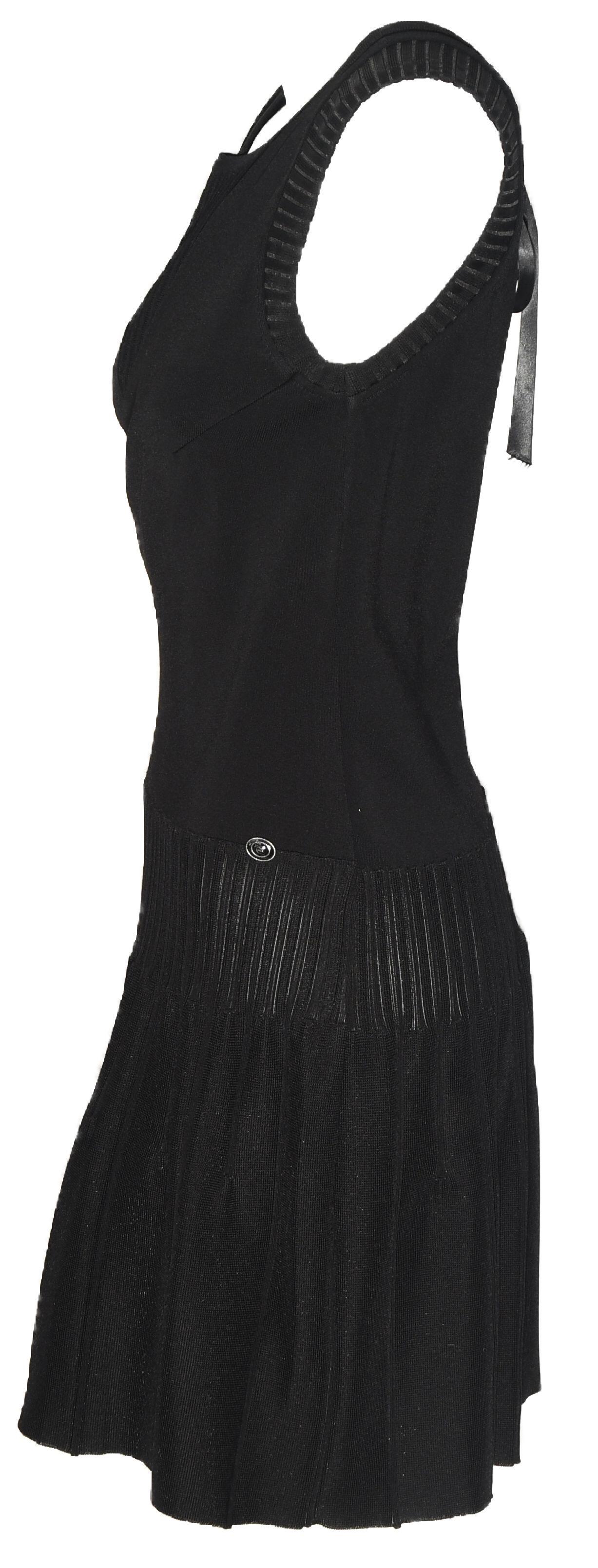 Chanel black sleeveless dress includes a V peek a boo back that is tied with a black satin bow.  This dress is ribbed at the front V neck and the slight drop sleeves.  With a drop waist to the hips this dress is gathered with mini ribbed pleats then