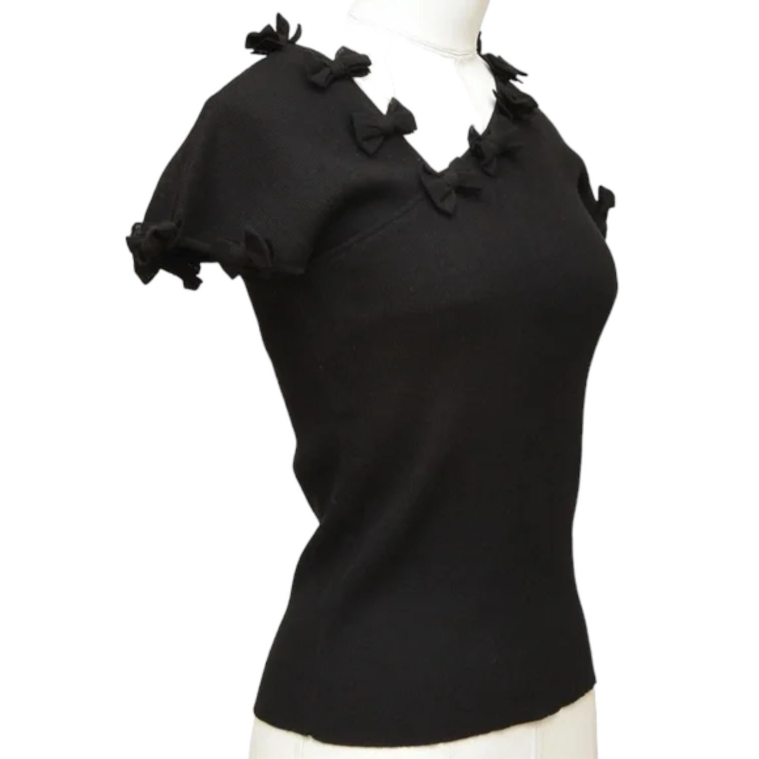 GUARANTEED AUTHENTIC CHANEL BLACK CAP SLEEVE KNIT

Design:
 - Cap sleeve black knit.
 - Off center v-neck.
 - Bow detail.
 - Pullover.
 - CC logo plaque at left hip.

Fabric: 82% Cotton, 18% Polyamide

Size: 36

Measurements (Approximate laid flat,