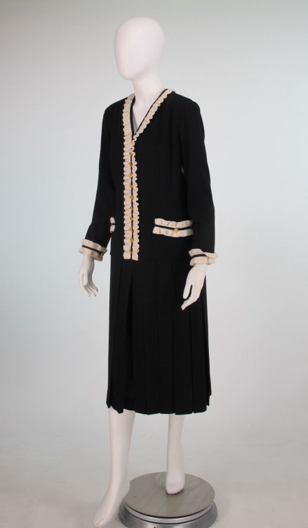 Chanel black & white knit long sleeve, dropped waist dress with pleated skirt, trimmed in white crochet wool, with gold camellia buttons at the front and cuff. Dress closes at the back with a zipper and hook/eye. From the 1980s. Marked size 40.
  