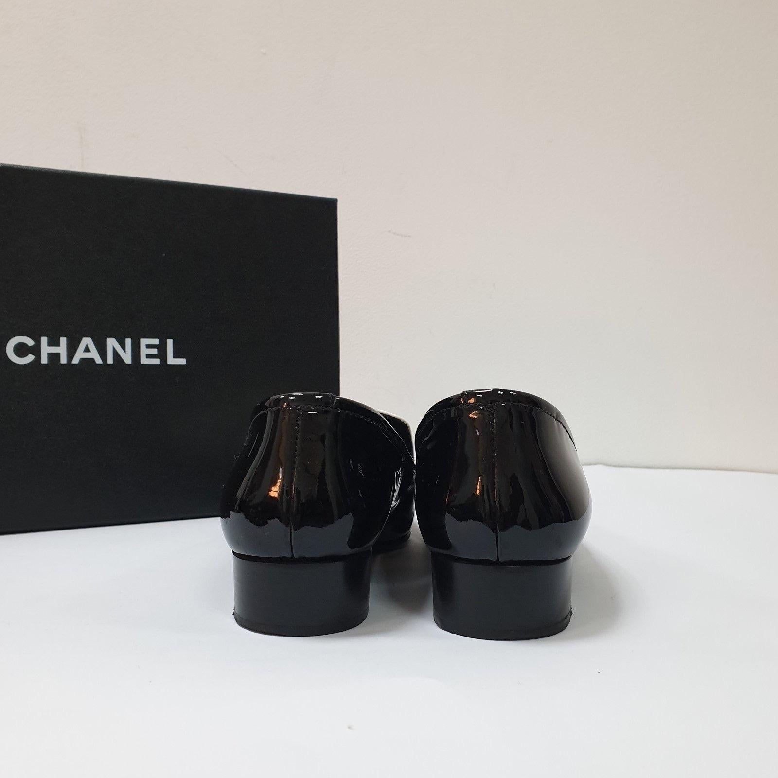 Sortez avec style grâce à ces superbes mocassins en cuir verni noir et blanc de Chanel ! Ces mocassins à enfiler sont une taille 37 et présentent un embellissement chic en maillons de chaîne CC. Ils sont en bon état, avec des signes d'usure comme le