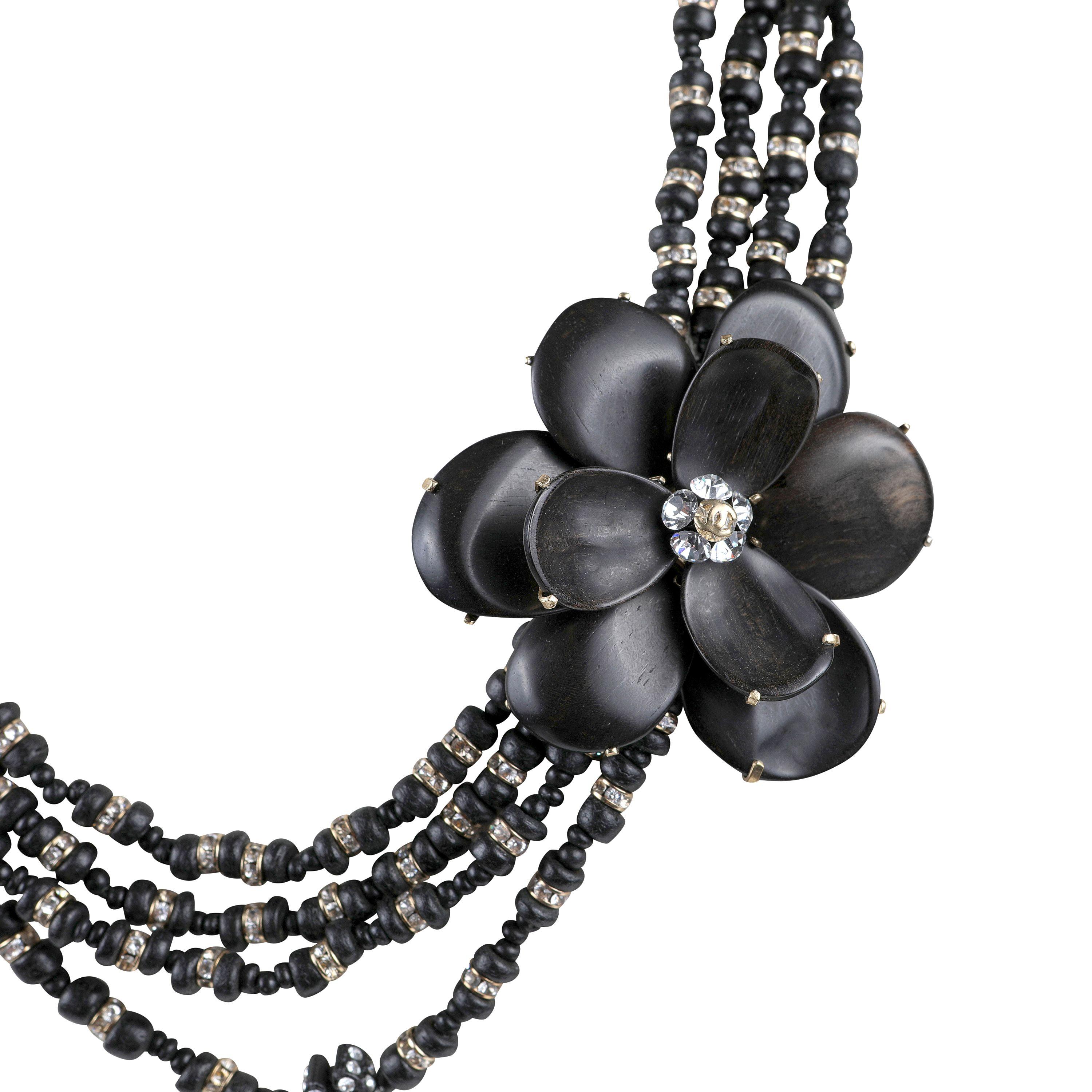 Diese authentische Chanel Schwarz Holzperlen und Kamelie Blume Halskette ist tadellos. Vier Reihen schwarzer Holzperlen sind mit funkelnden Kristallen durchsetzt.   Eine große Kamelienblüte hält die verschiedenen Stränge zusammen.  Inklusive Tasche