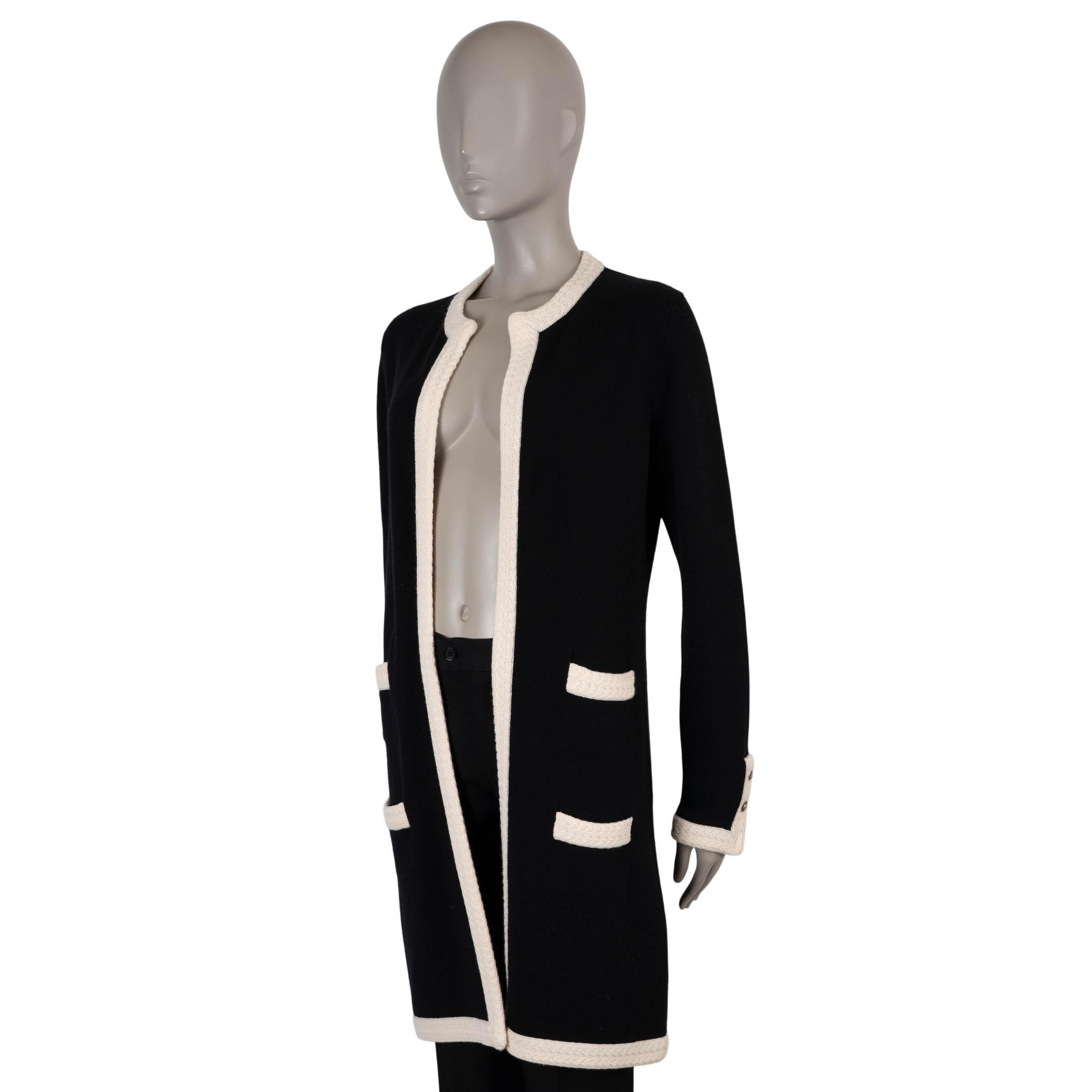 Questo cappotto in maglia Chanel, autentico al 100%, è realizzato in cashmere nero (100%) con finiture a contrasto color crema per un effetto bicolore senza tempo. Disegnato con una silhouette rilassata e lunga fino al ginocchio, presenta quattro